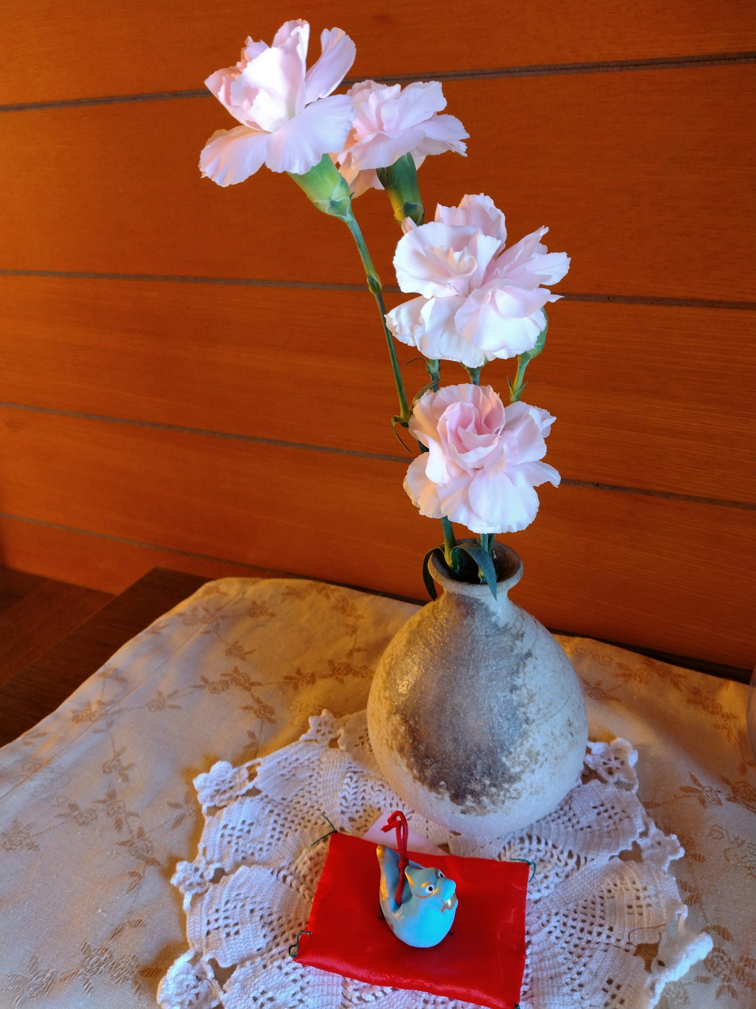 Vaso in ceramica con garofani rosa e una piccola decorazione di uccello blu su un tessuto rosso