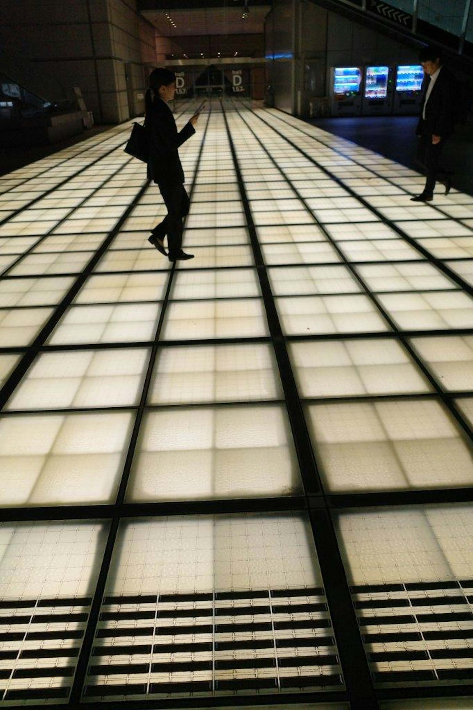 Personas caminando sobre un suelo con patrón de cuadrícula brillante