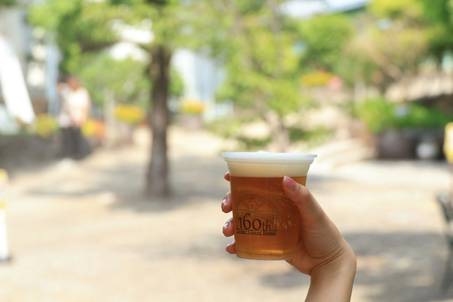 Una mano che tiene un bicchiere di birra con uno sfondo sfocato di verde