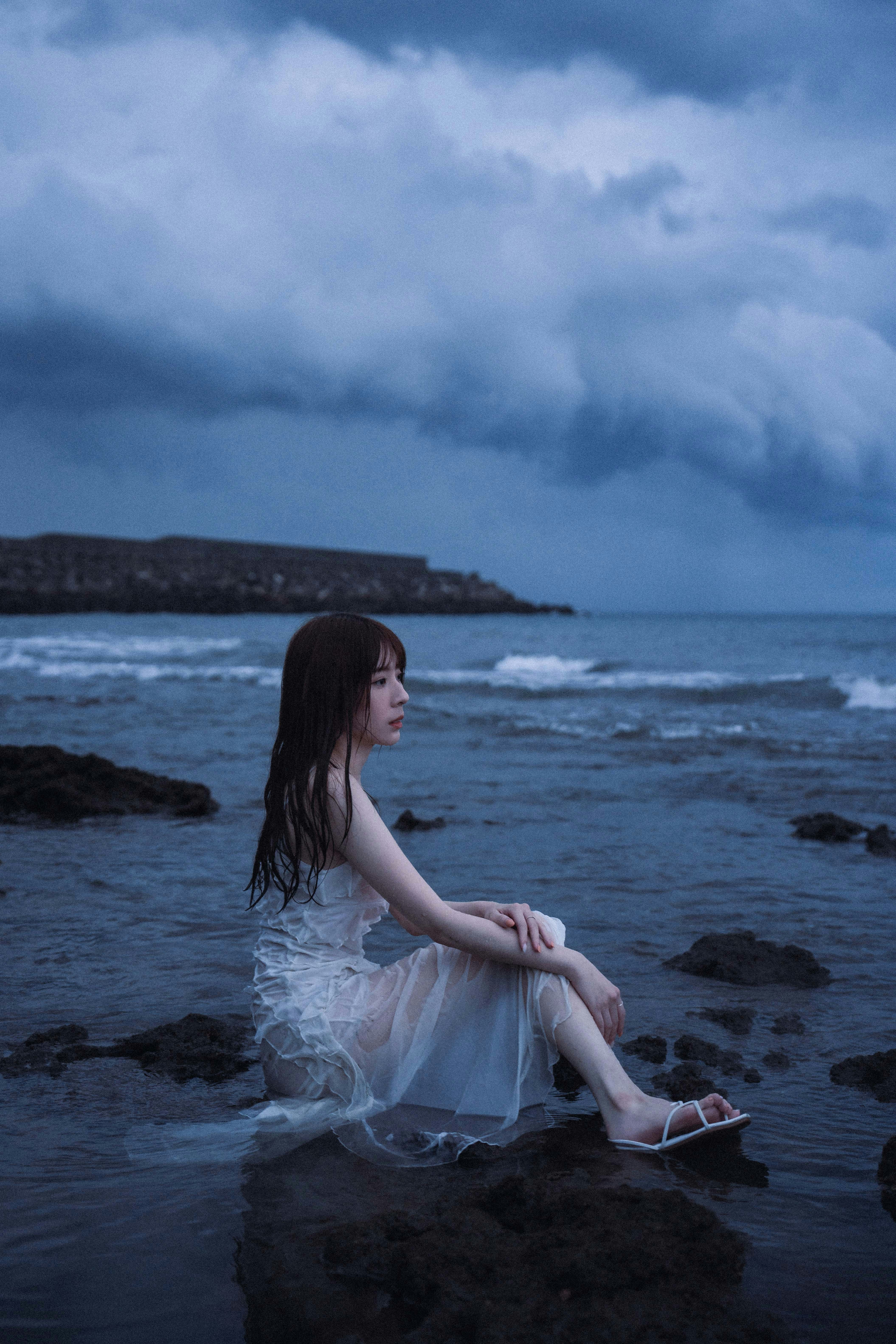 海辺の岩場で座る女性と青い空の風景