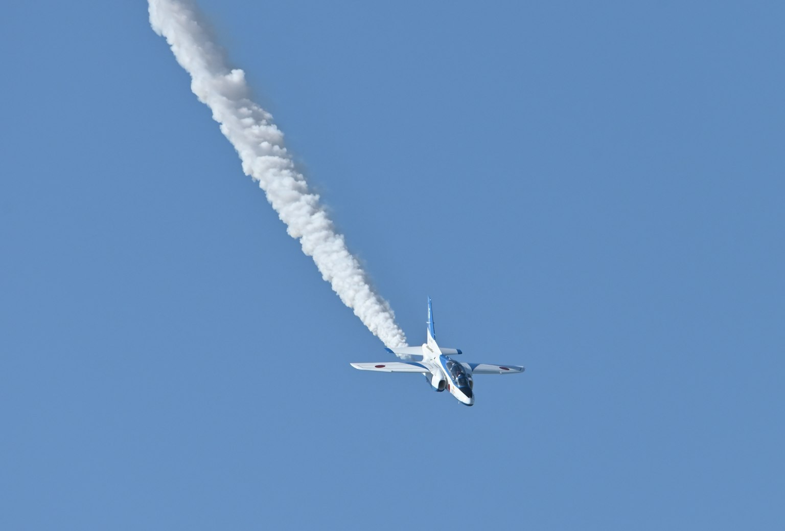 Un avión volando contra un cielo azul con una estela blanca detrás