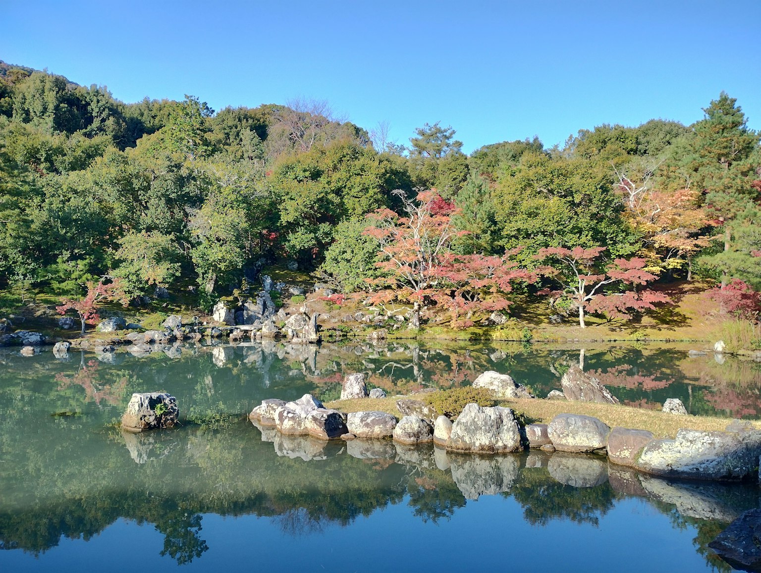 Paisaje sereno con un estanque y árboles coloridos reflejados en el agua
