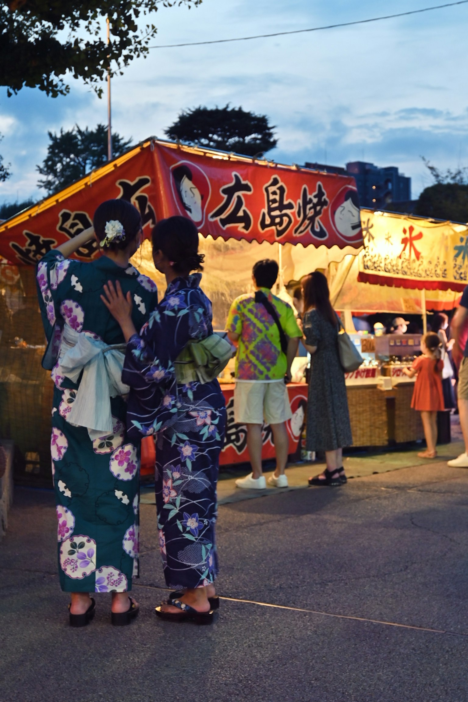 Women in kimono at a summer festival standing in front of food stalls