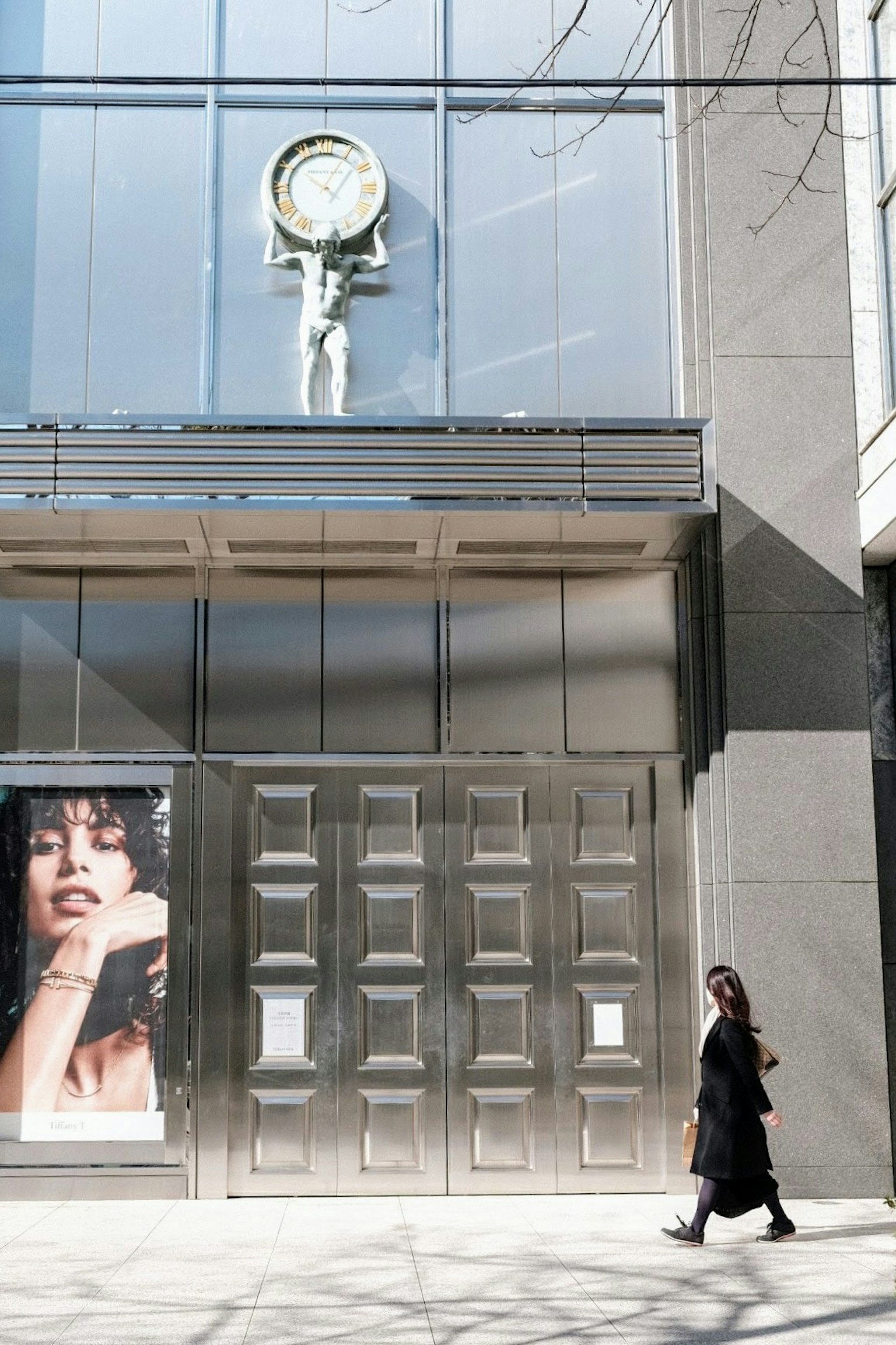 Esterno di un edificio moderno con un grande orologio e una donna in nero che passeggia
