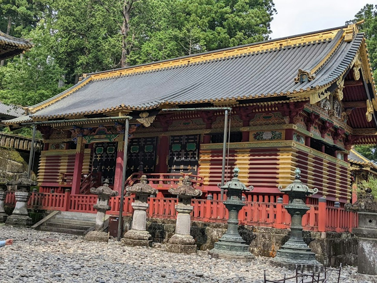 Hermoso edificio de santuario japonés con decoraciones rojas y doradas rodeado de vegetación y faroles de piedra
