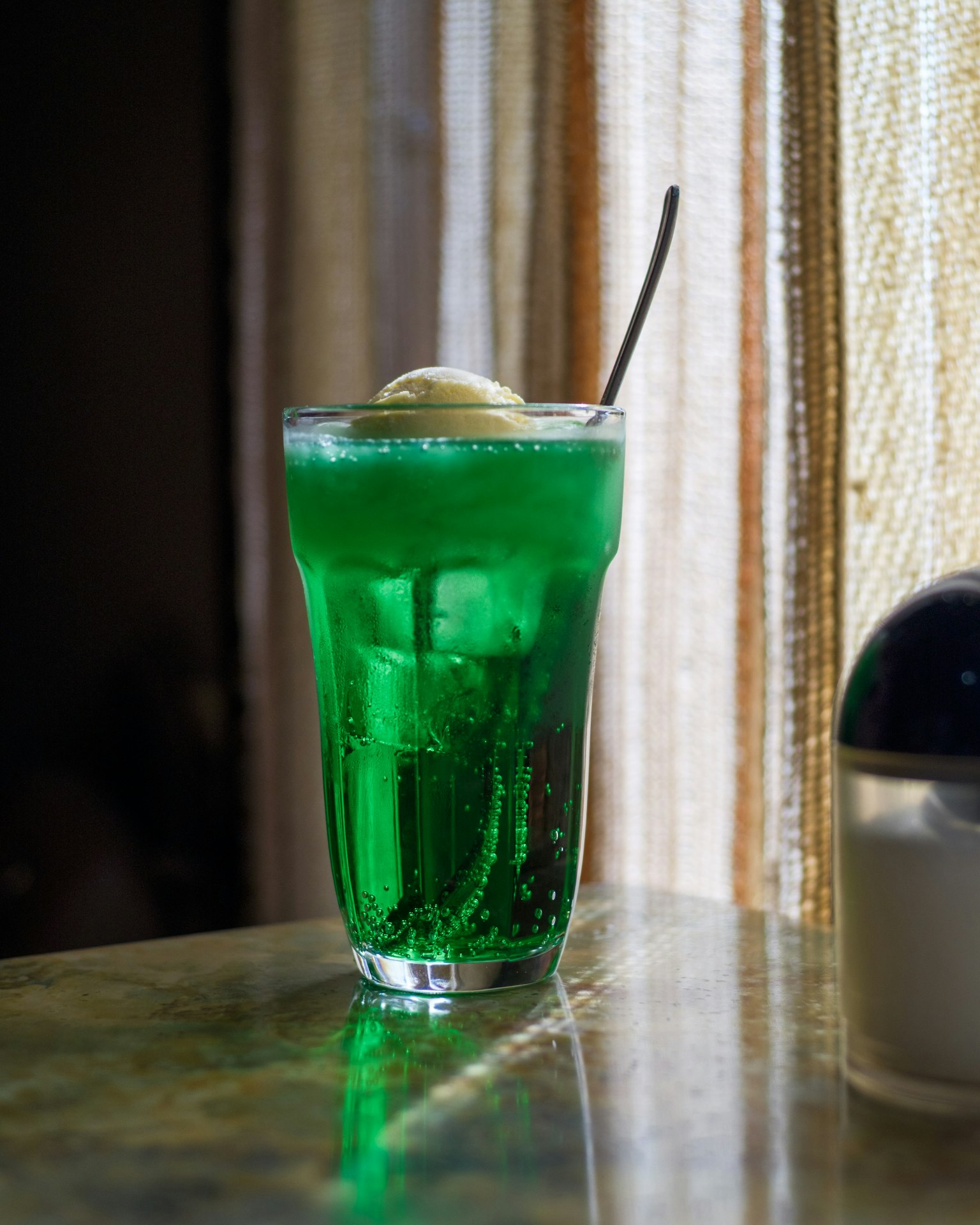 緑色の炭酸飲料とアイスクリームの入ったグラスが窓際に置かれている