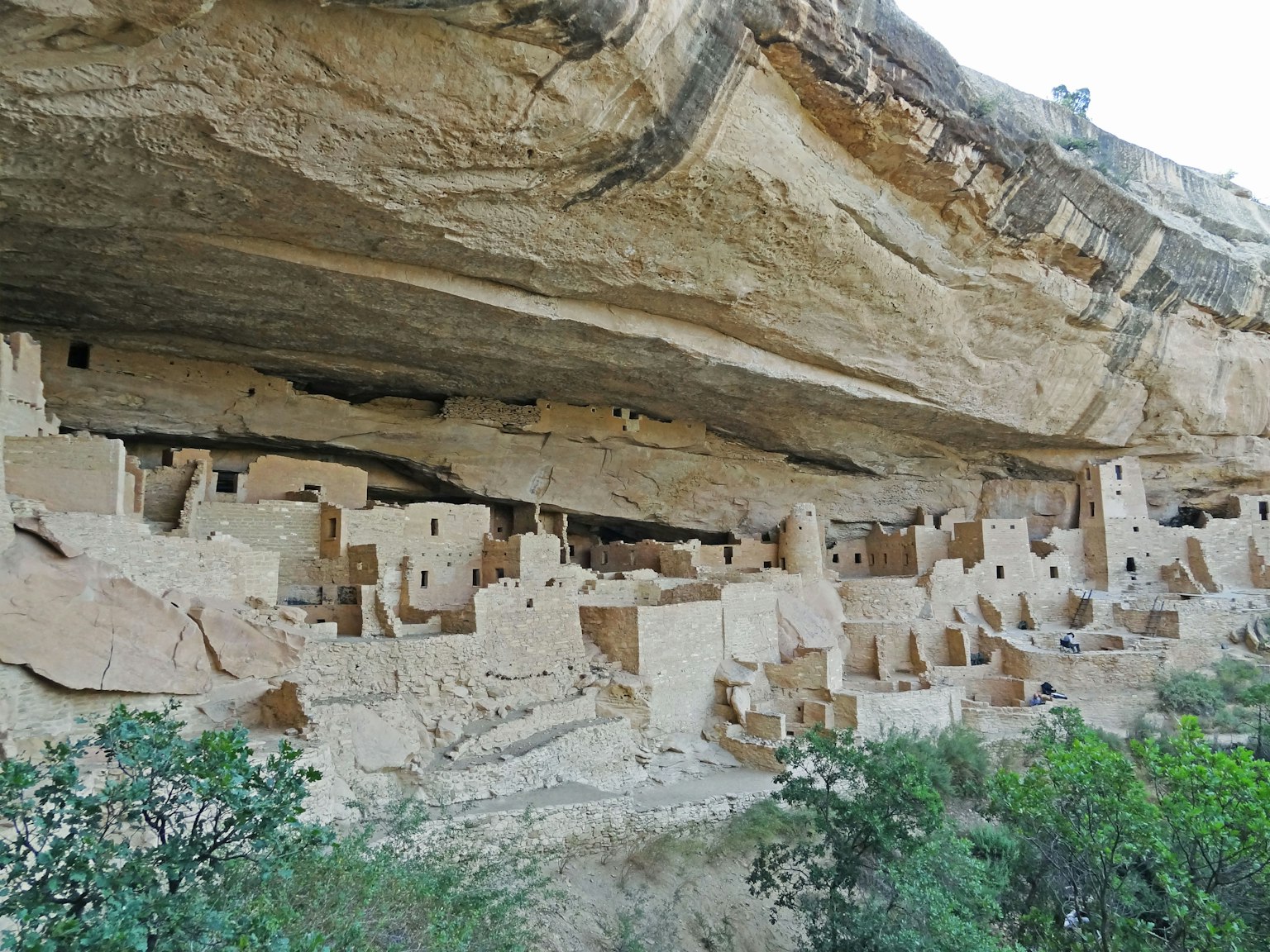 Antike Wohnungen unter einer Klippe mit Sandsteinstrukturen und umliegendem Grün