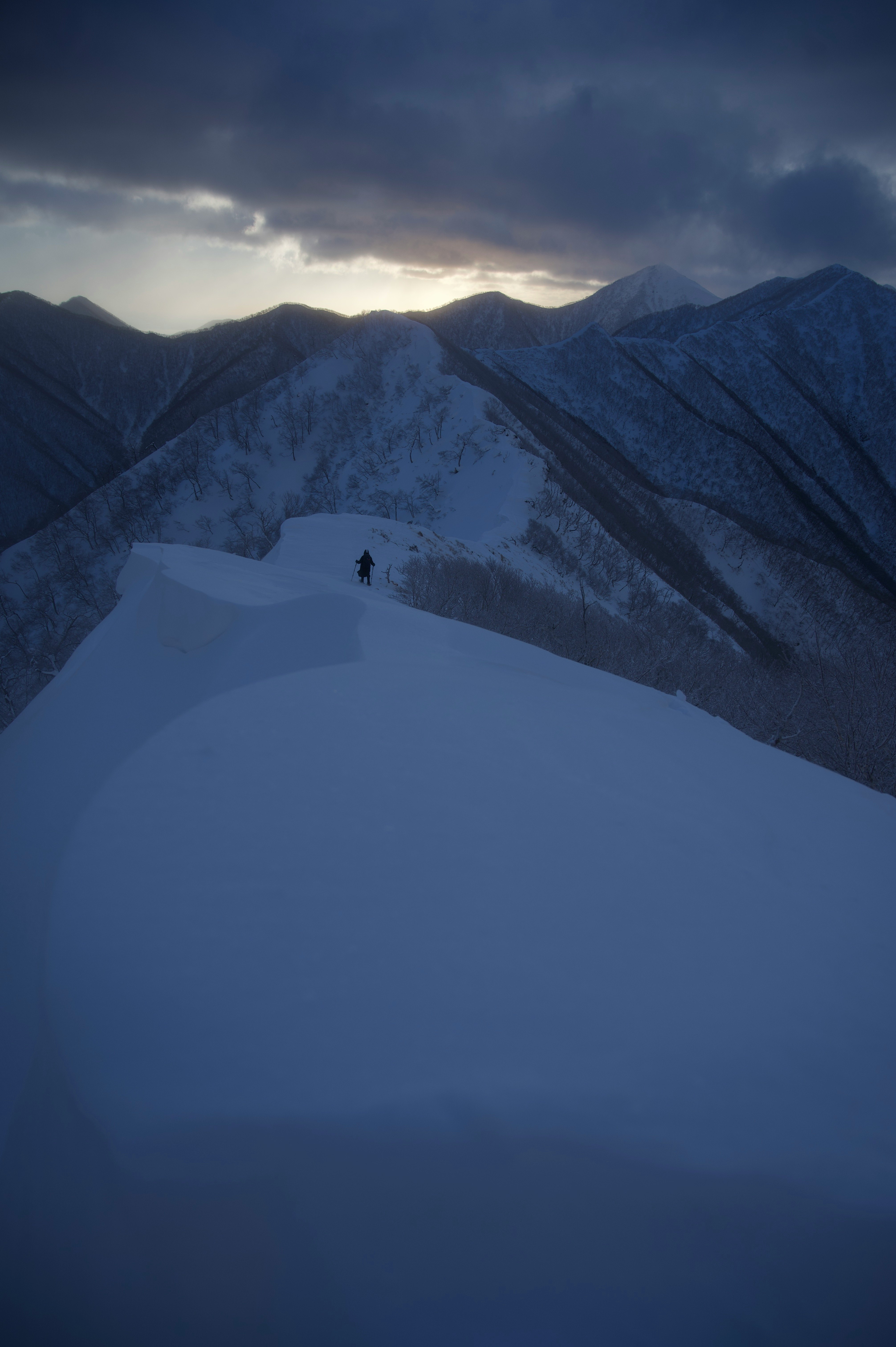 雪原を歩く人と山並みの夕暮れ