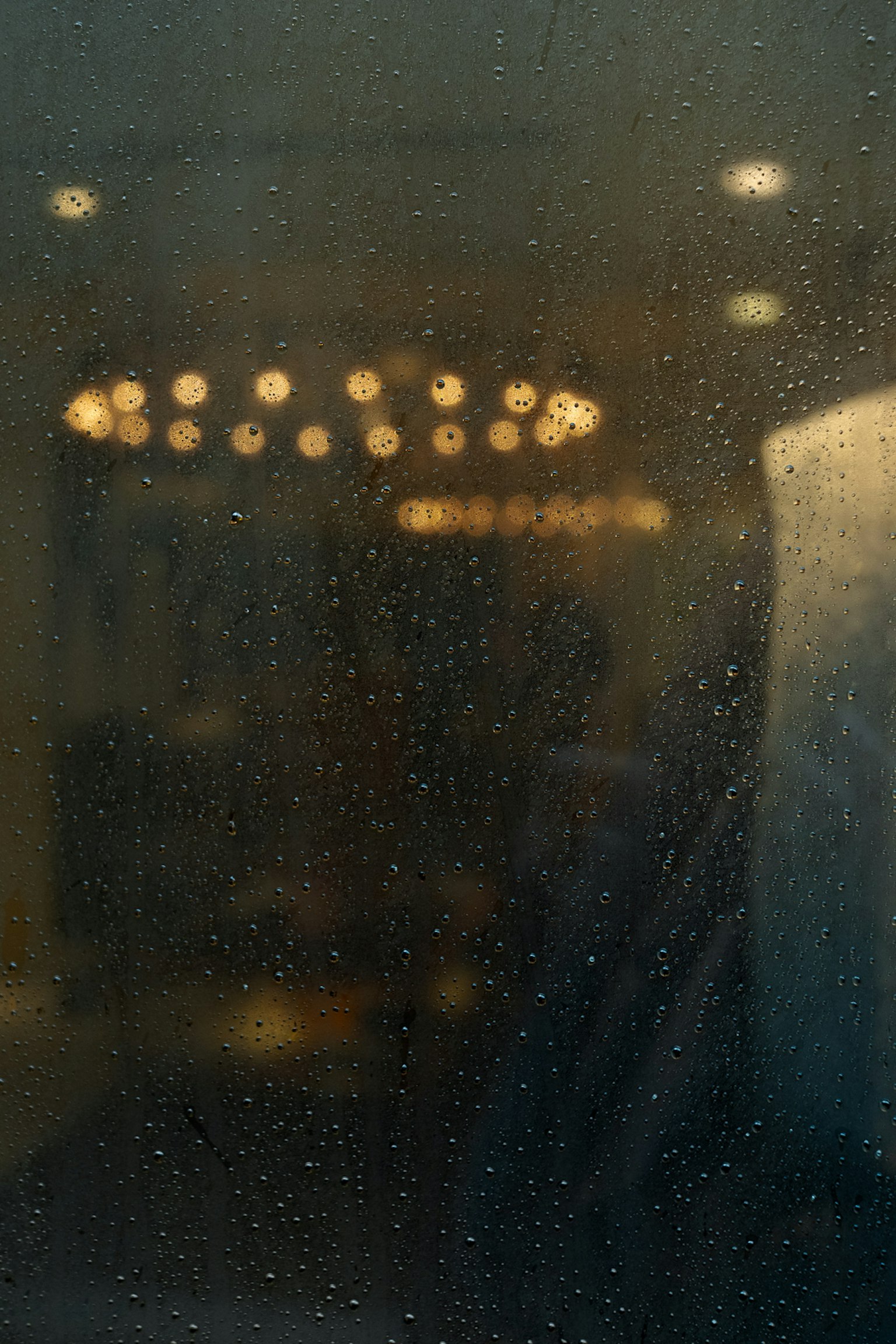 Blurred chandelier lights seen through a rain-speckled window