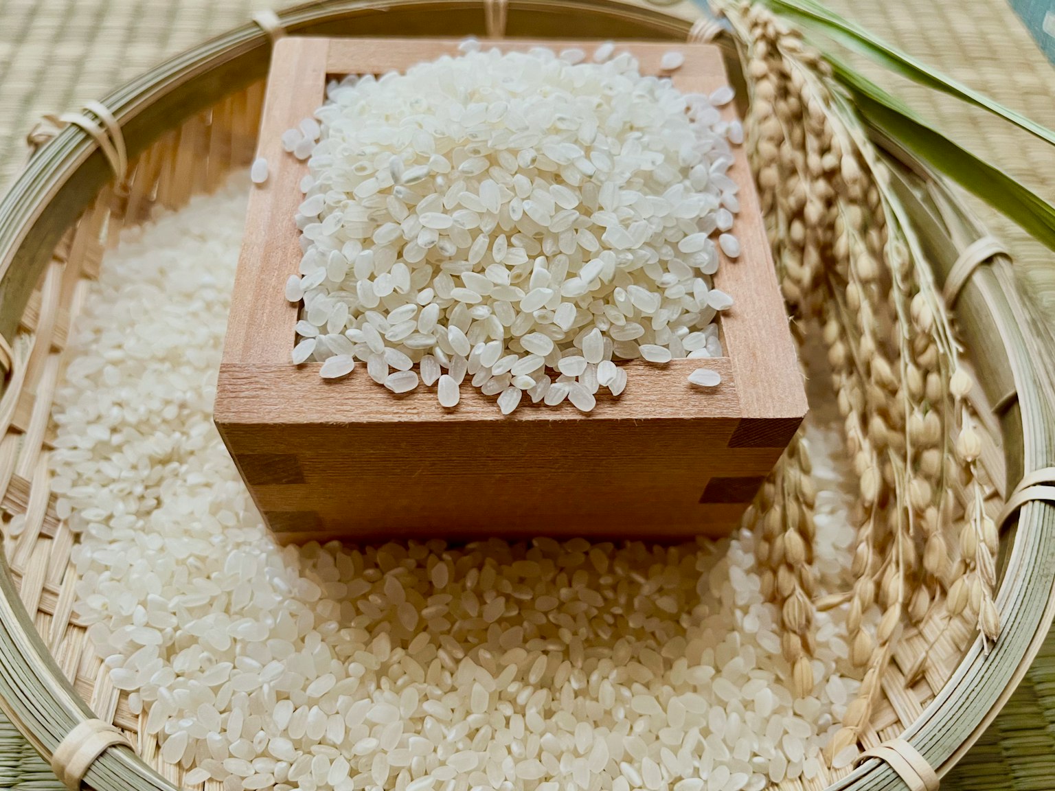 White rice heaped in a wooden container surrounded by scattered rice grains