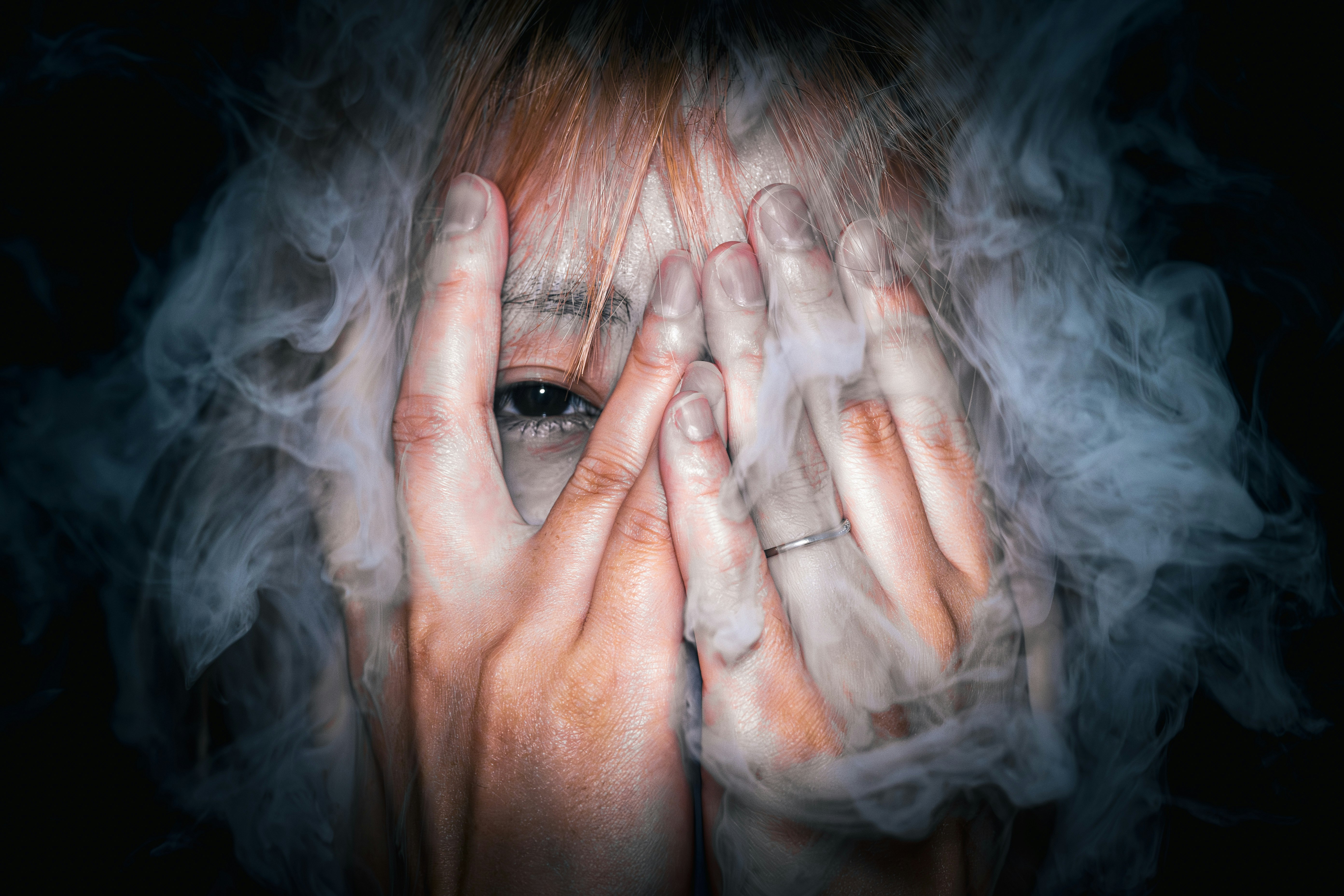 person covering eyes with hands in swirling smoke