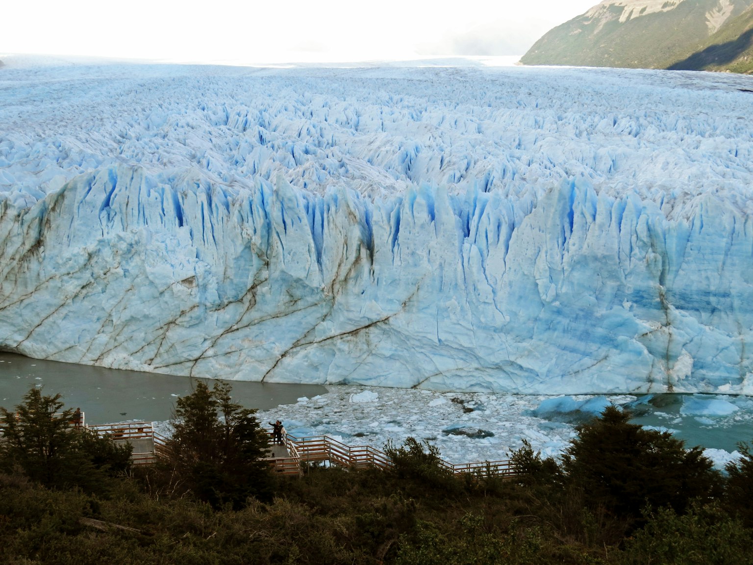Un immense mur de glacier bleu avec des crevasses et une rivière en contrebas