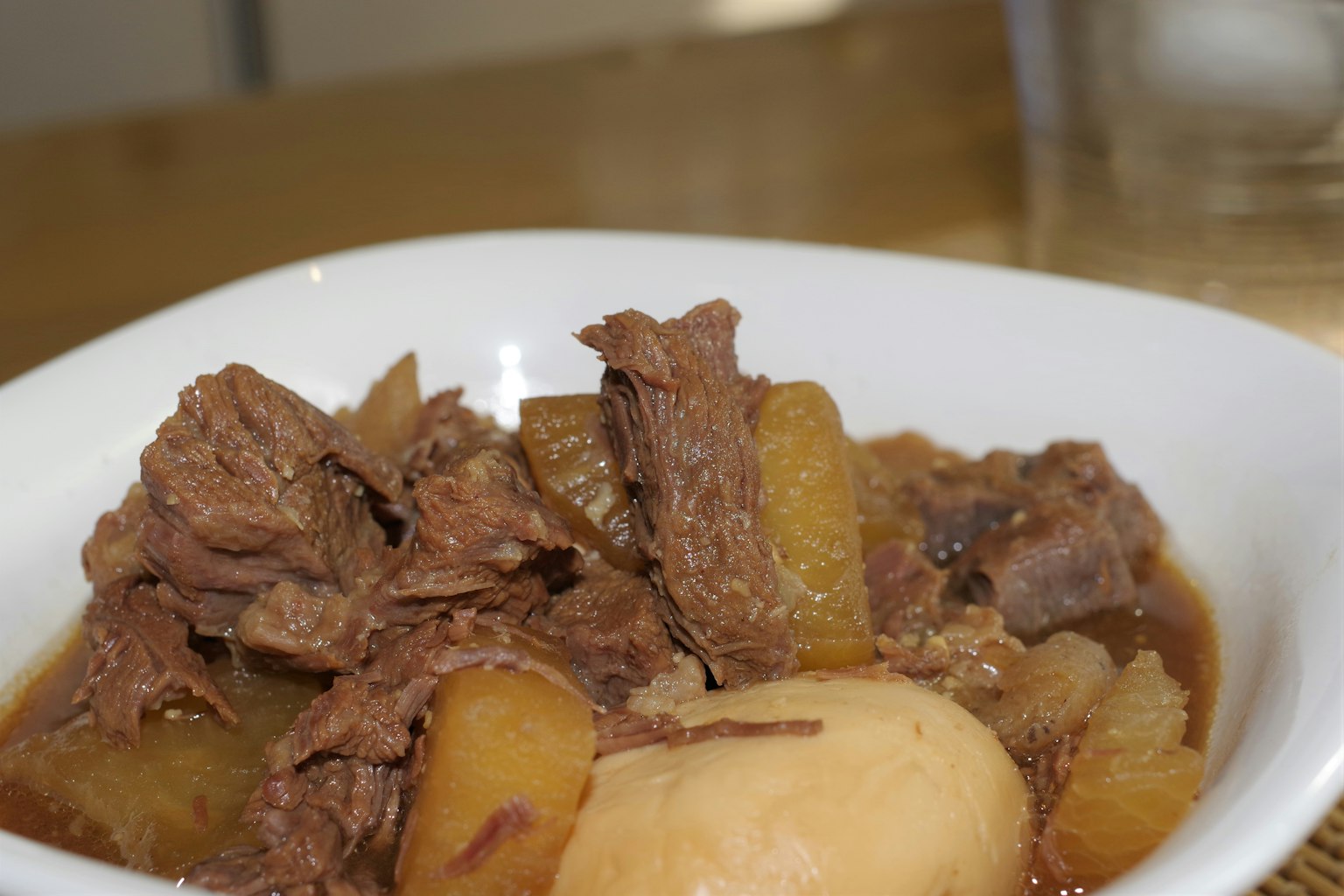 Un bol blanc rempli de ragoût de boeuf et de légumes avec des morceaux de viande et de pommes de terre