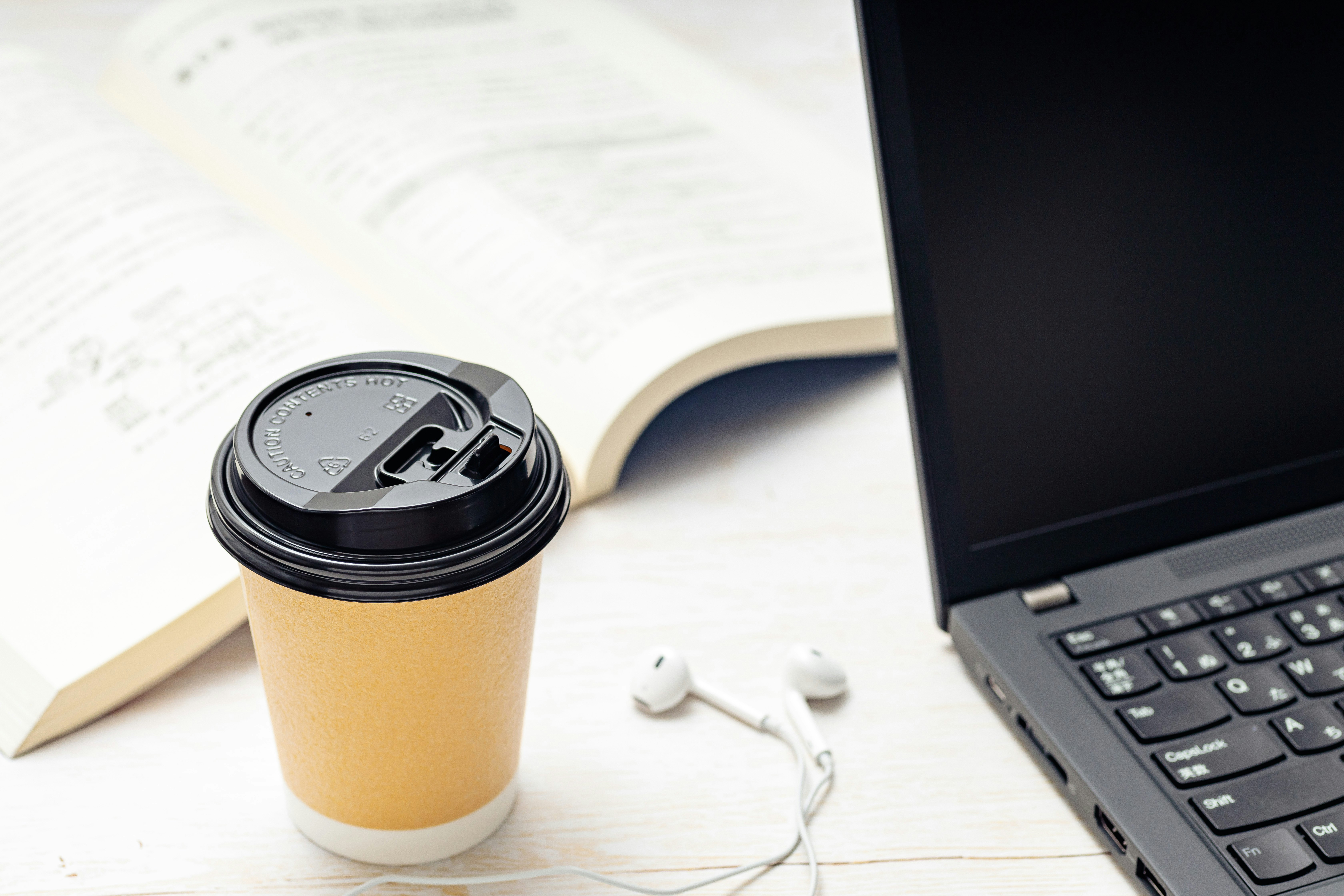 コーヒーとイヤホン、書籍とPCが並ぶデスク