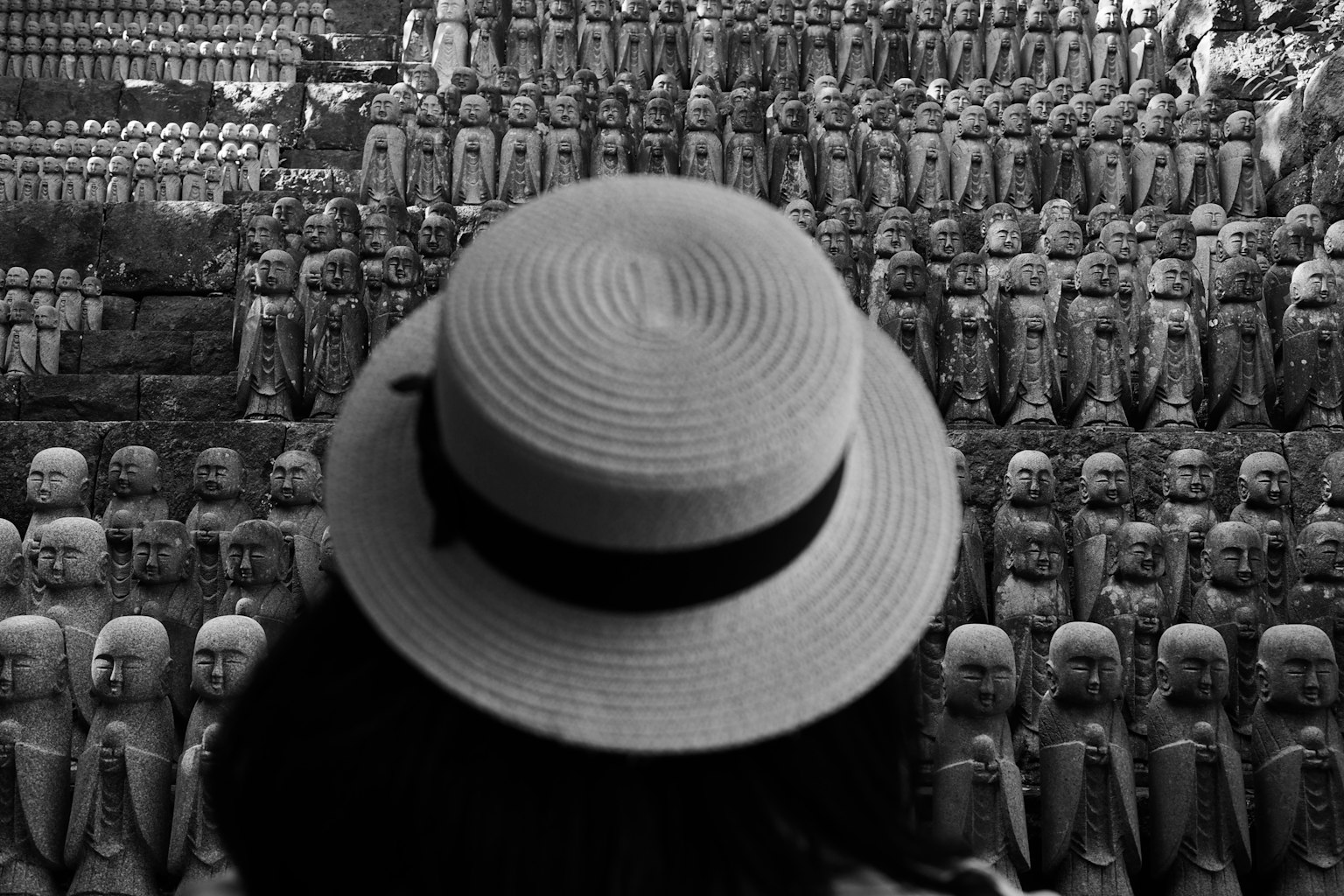 모자를 쓴 사람이 단색 배경에서 수많은 석상을 바라보고 있는 모습