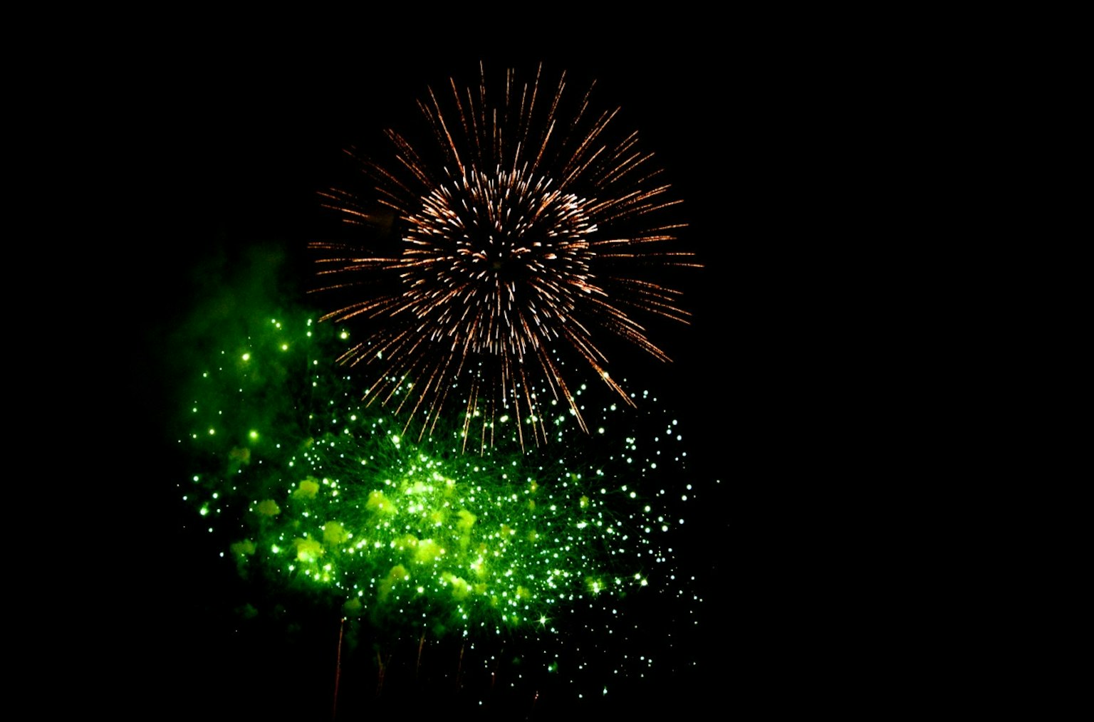 Hermoso momento de fuegos artificiales verdes y dorados que explotan sobre un fondo negro