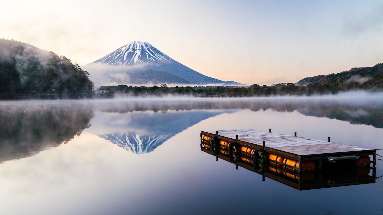 Vista serena de un lago reflejando el monte Fuji con una atmósfera brumosa al amanecer