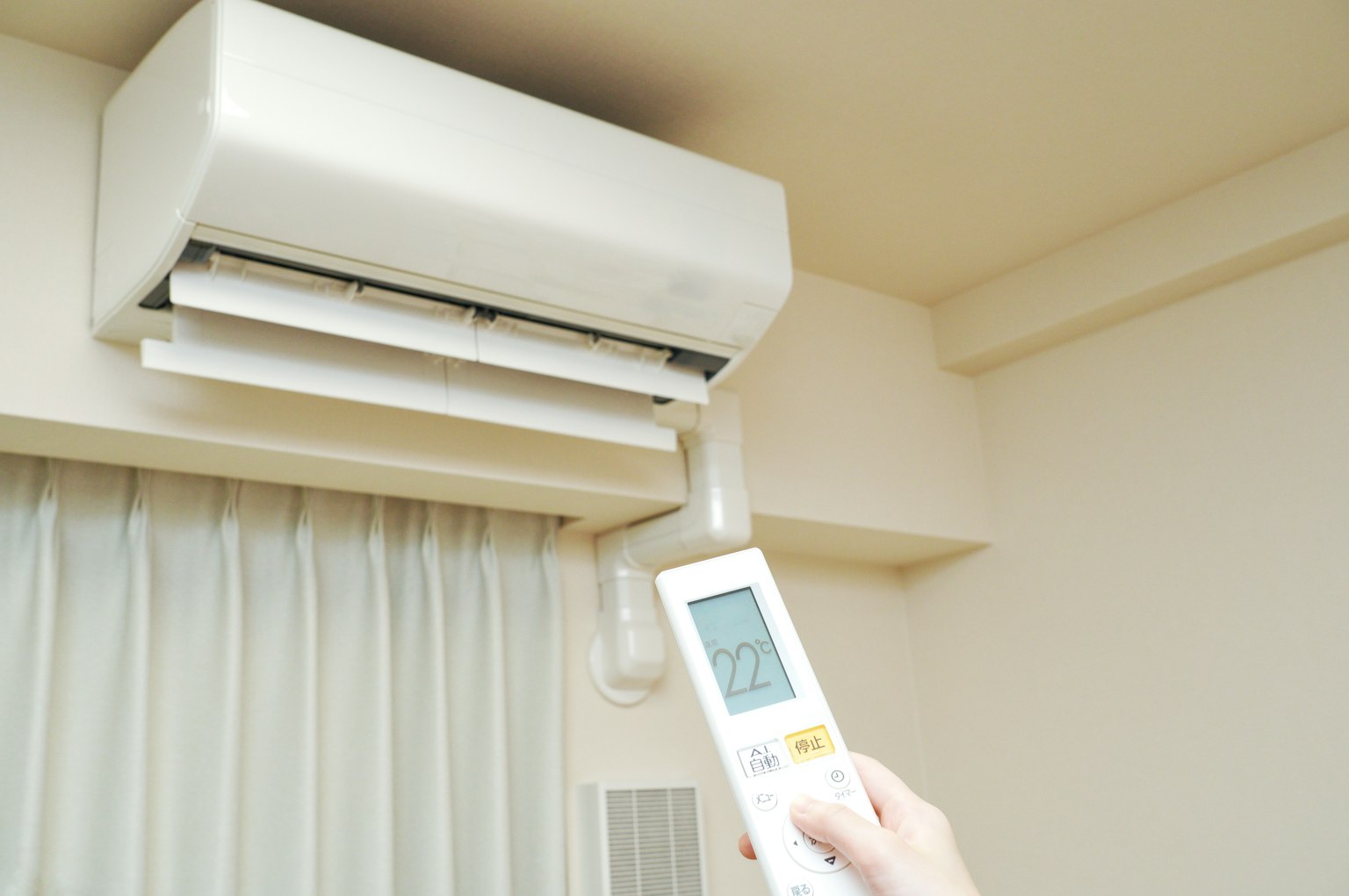 Image intérieure montrant un climatiseur et une main tenant une télécommande