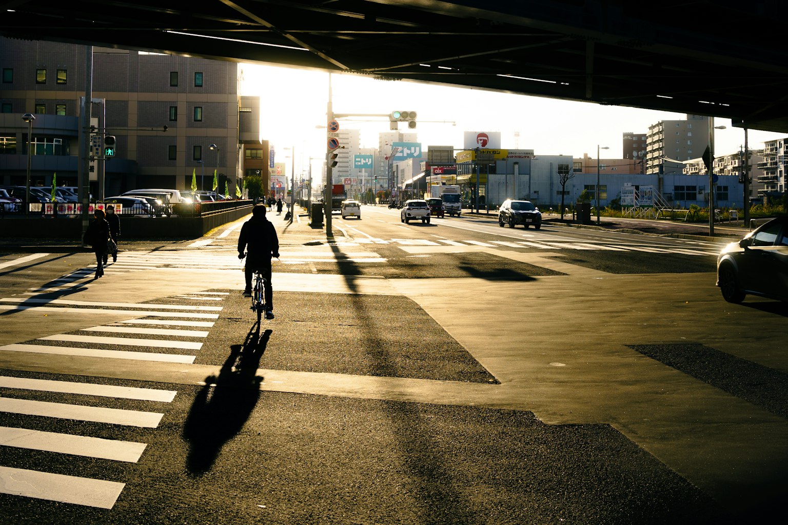 Silhouette of a cyclist and pedestrians at a crosswalk during sunset