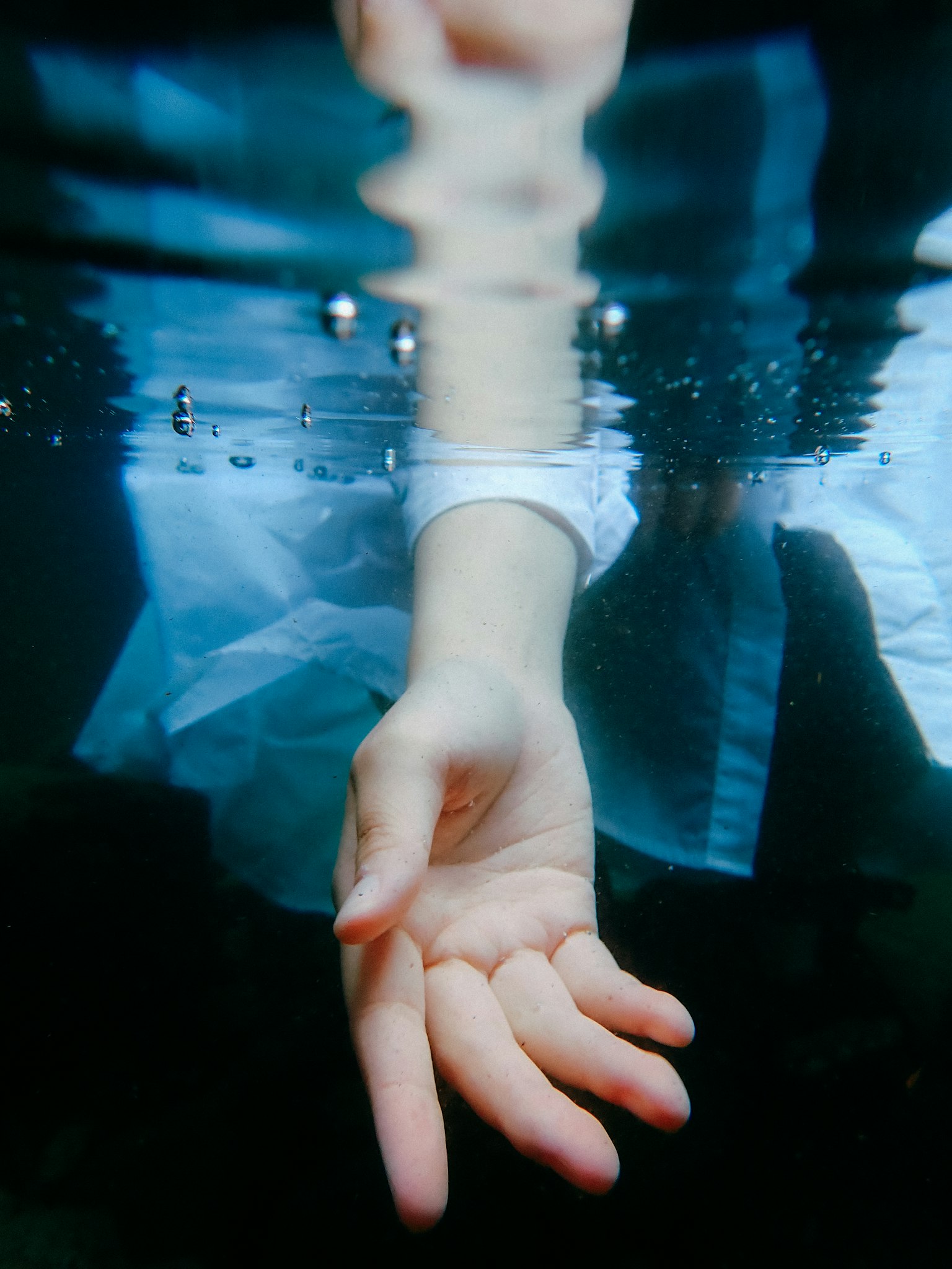 A hand reaching out underwater with reflections on the surface