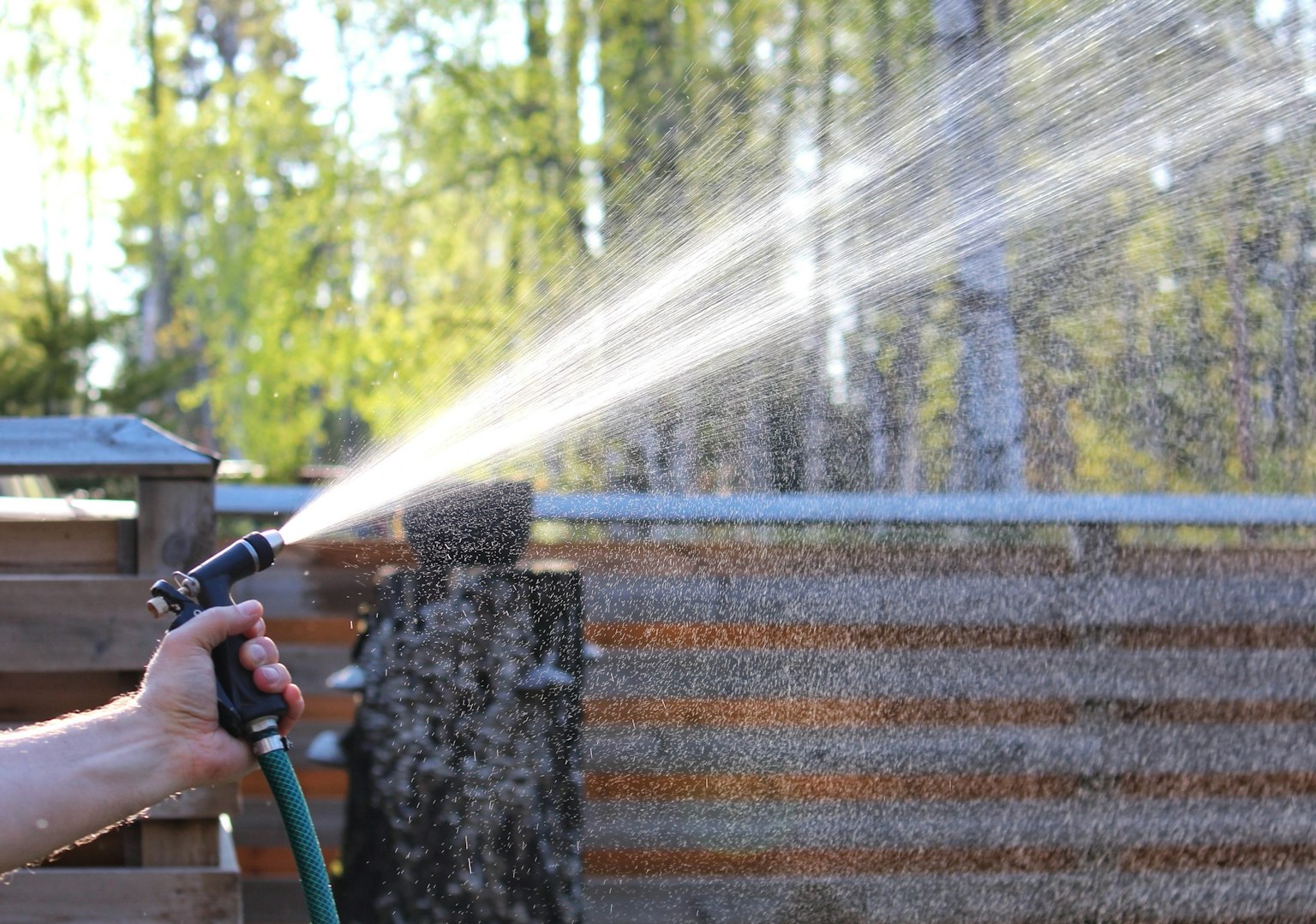 水を撒いているホースの手元 背景に緑の木々