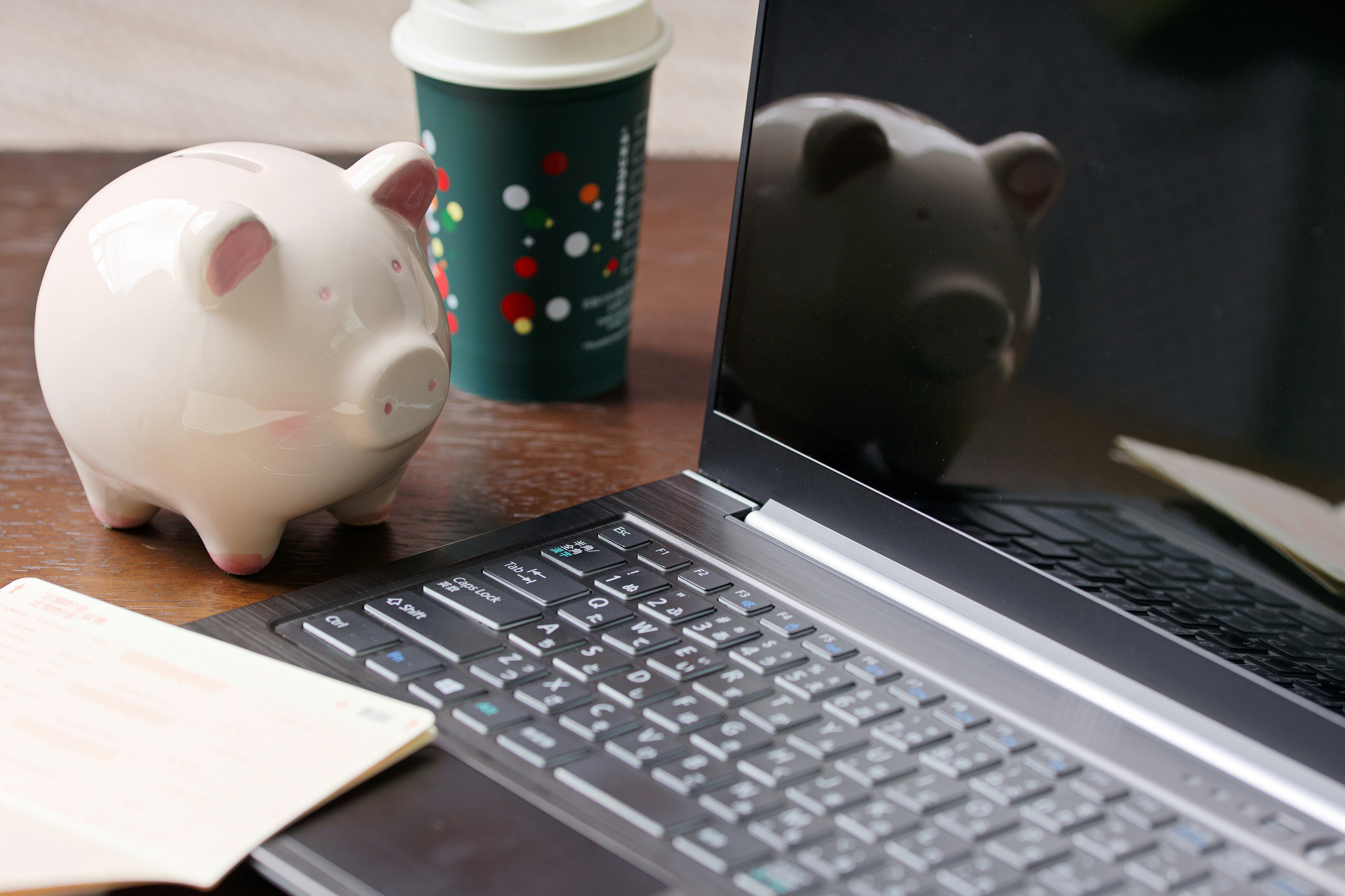 ノートPCと貯金箱、コーヒーと通帳が並ぶデスク