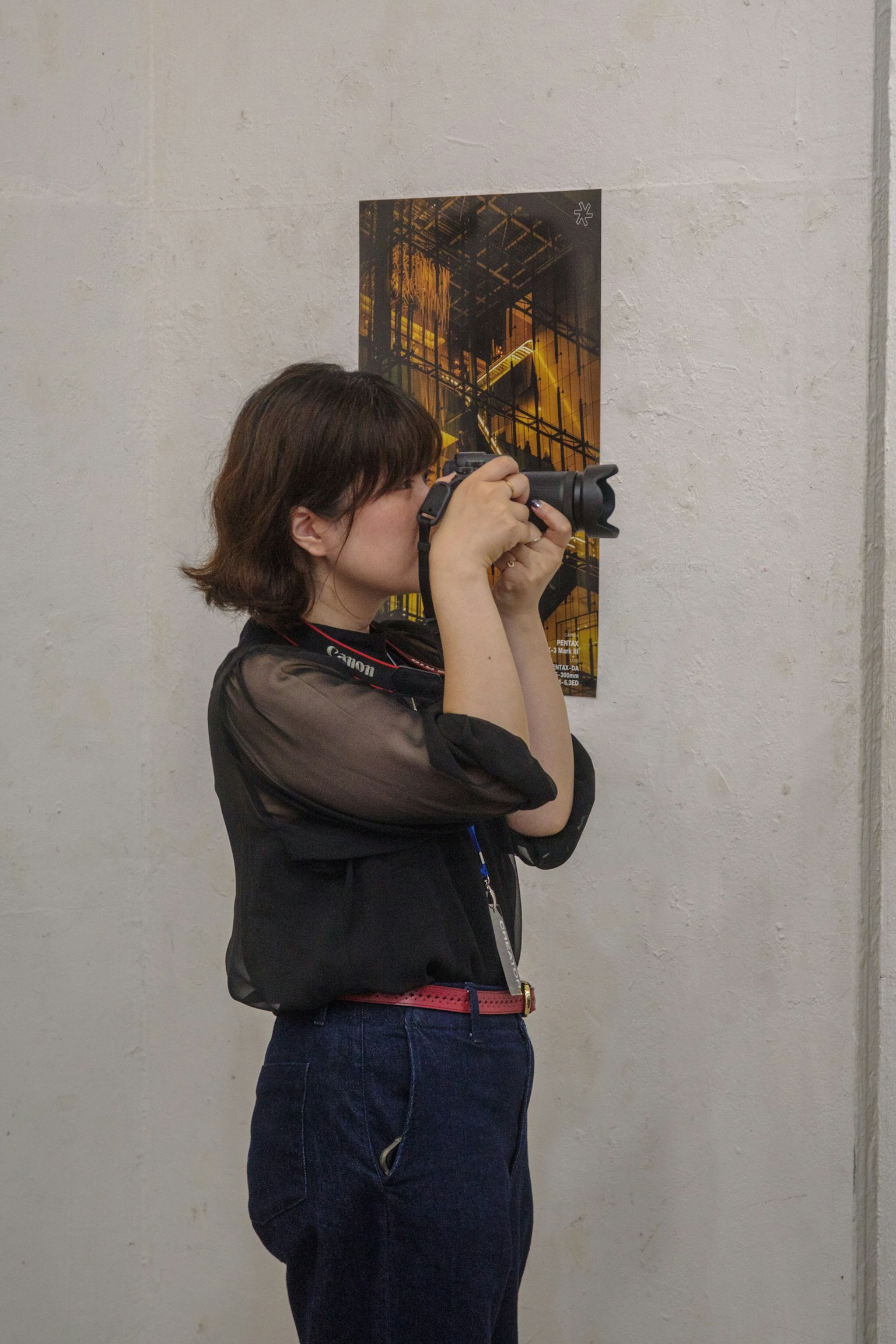 카메라로 사진을 찍고 있는 여성의 측면 모습 배경에 전시된 예술 작품