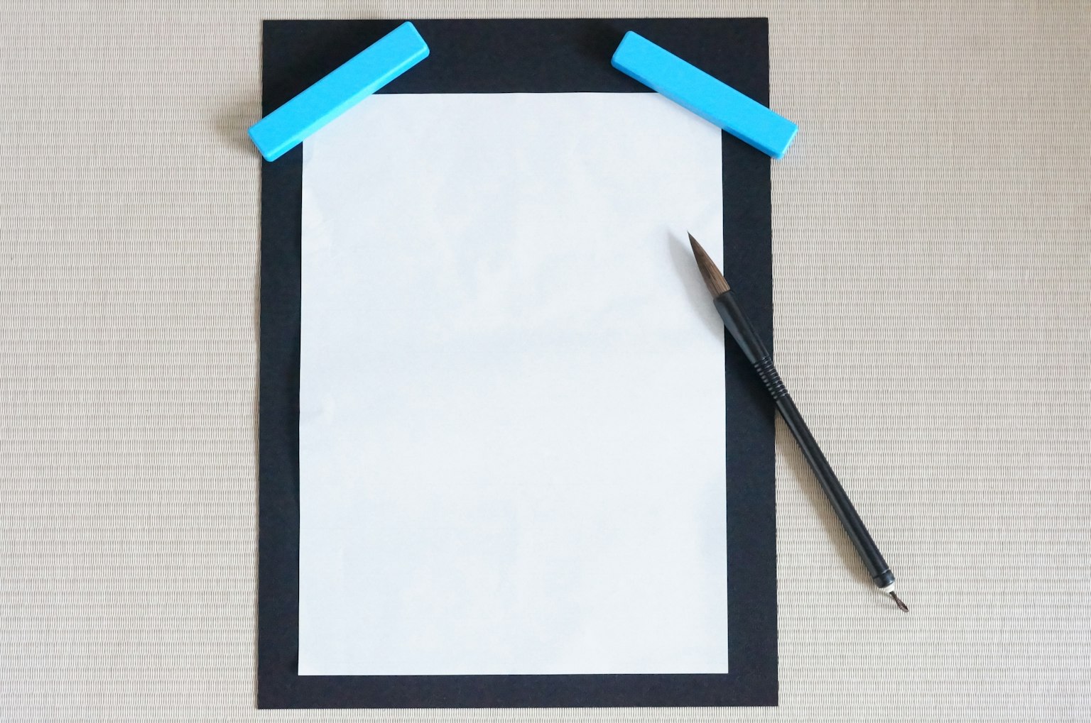 Ein leeres Blatt weißes Papier mit einem schwarzen Rahmen und blauen Clips, die es zusammen mit einem Stift halten