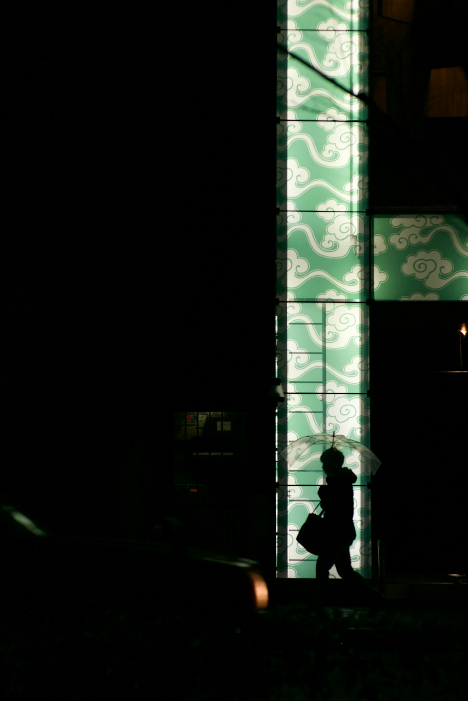 Silhouette of a person walking against a glowing green patterned wall in a dark setting