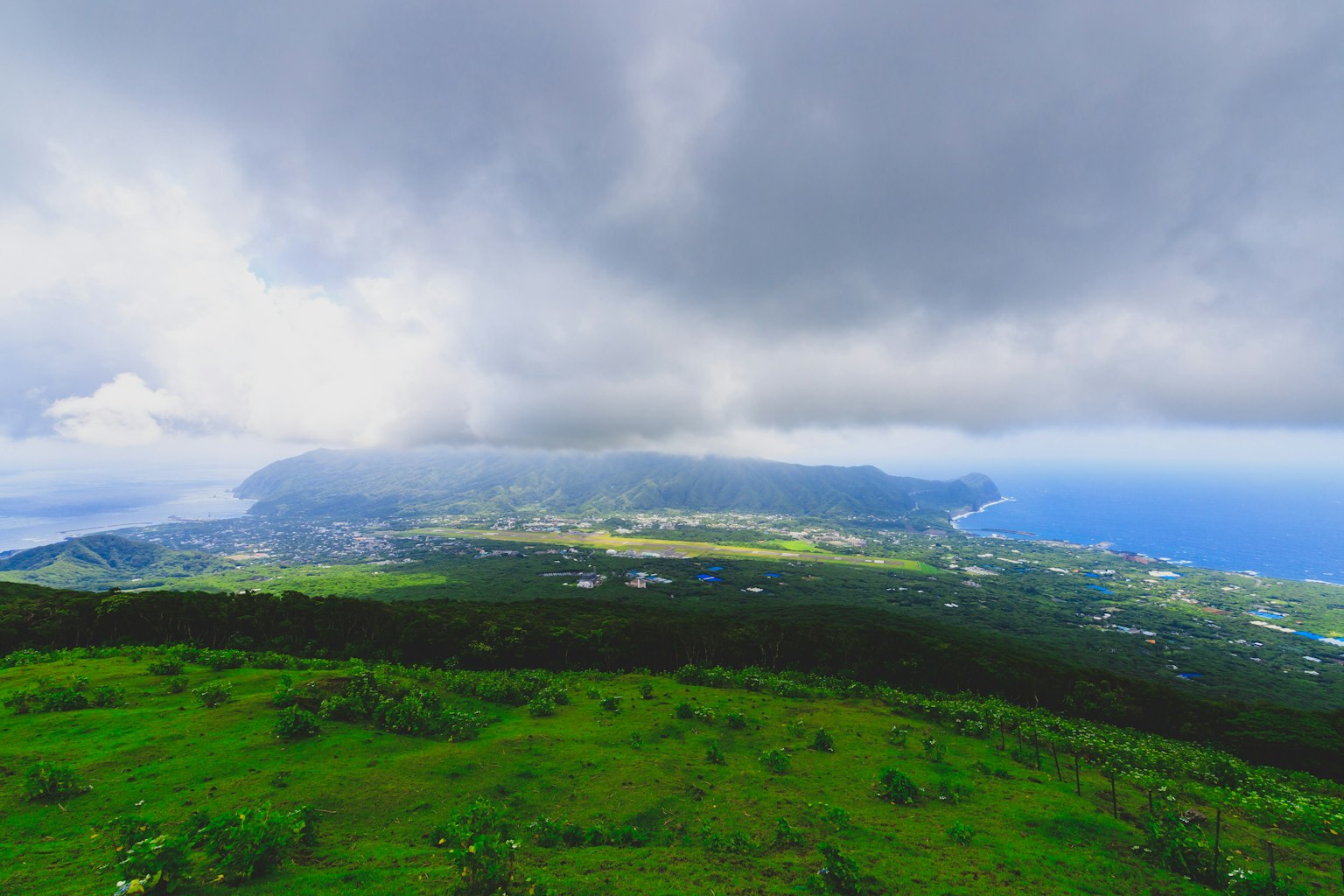Panoramablick auf die Küste von einem grünen Hügel mit bewölktem Himmel und fernen Inseln