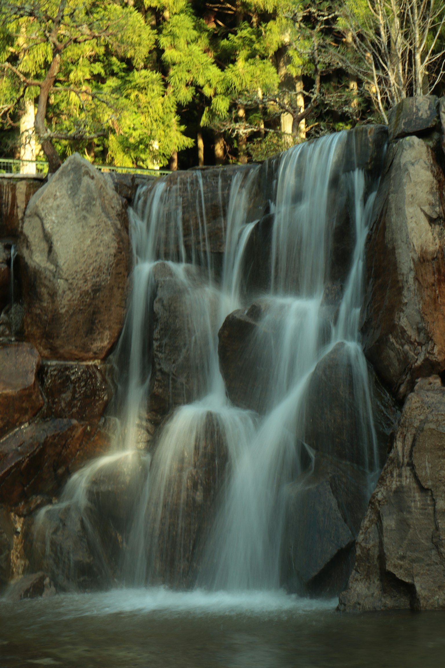 Air terjun tenang mengalir di atas batu dikelilingi pepohonan