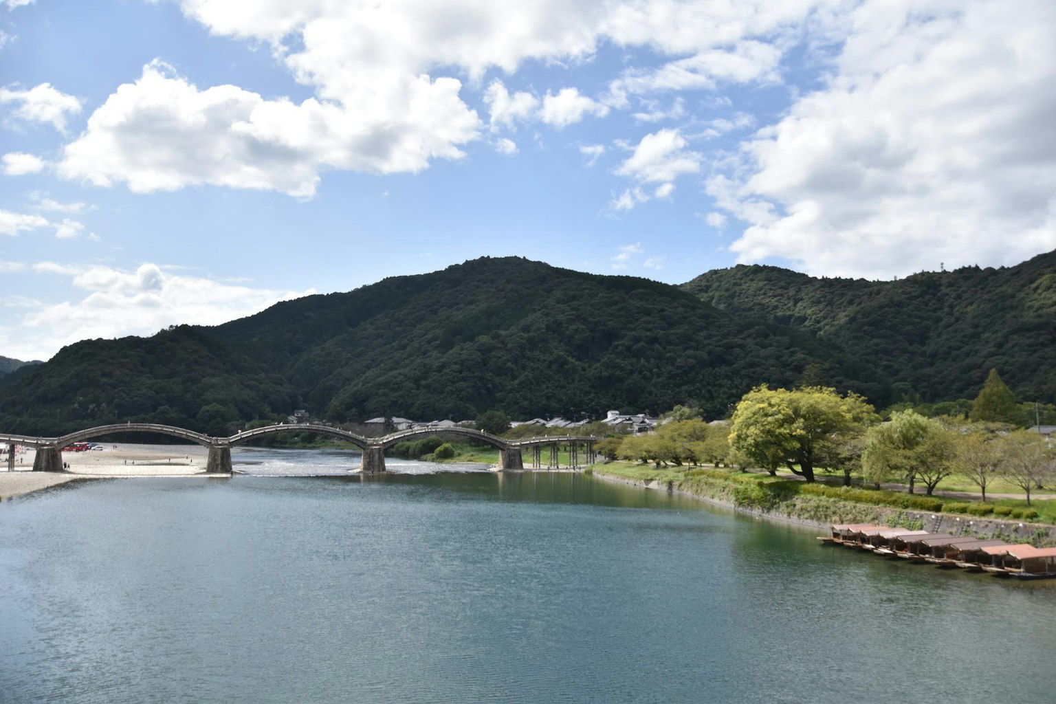 Vue pittoresque d'une rivière avec un pont en pierre entouré de montagnes vertes