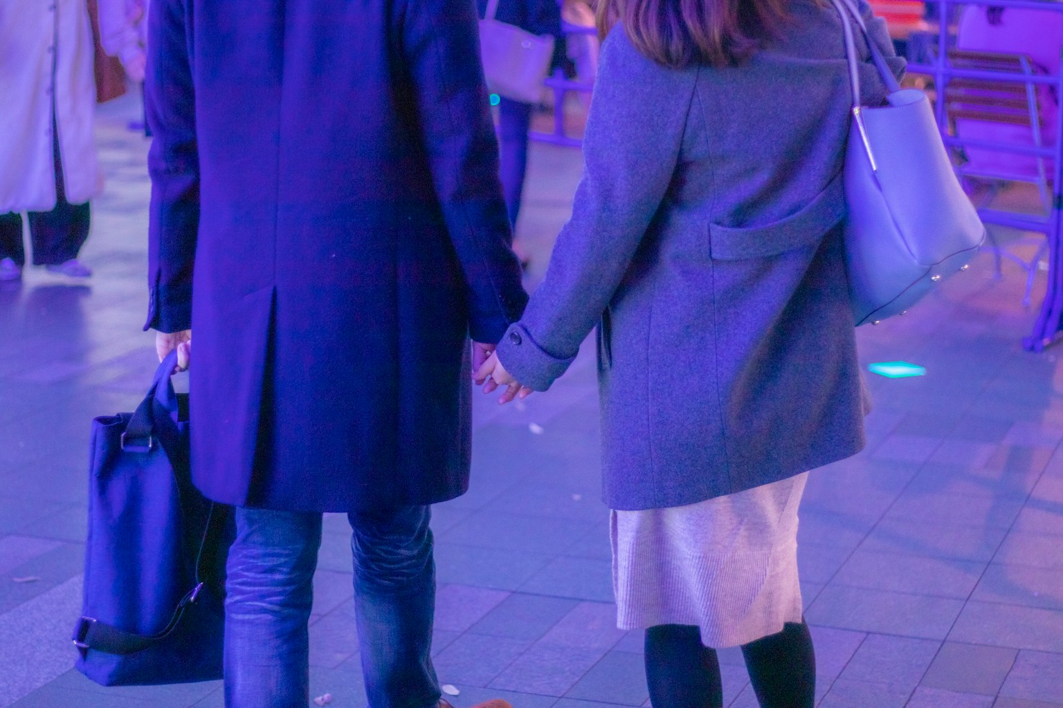 Cặp đôi nắm tay nhau đi bộ trong khu vực ánh sáng mờ mặc áo khoác xanh và xám