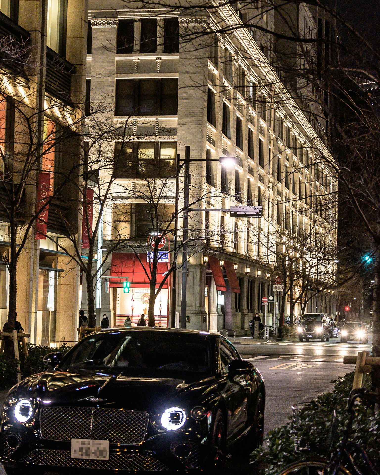 Một chiếc Bentley đen đậu trên đường phố thành phố vào ban đêm với các tòa nhà được chiếu sáng