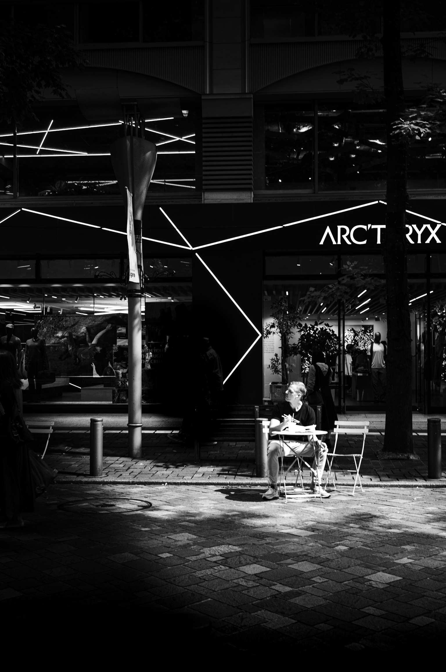 Seseorang duduk di depan toko Arc'teryx dengan pencahayaan yang unik