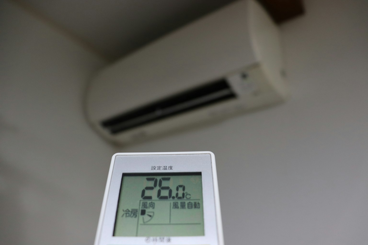Fernbedienung der Klimaanlage zeigt 26 Grad mit montierter Klimaanlage im Hintergrund
