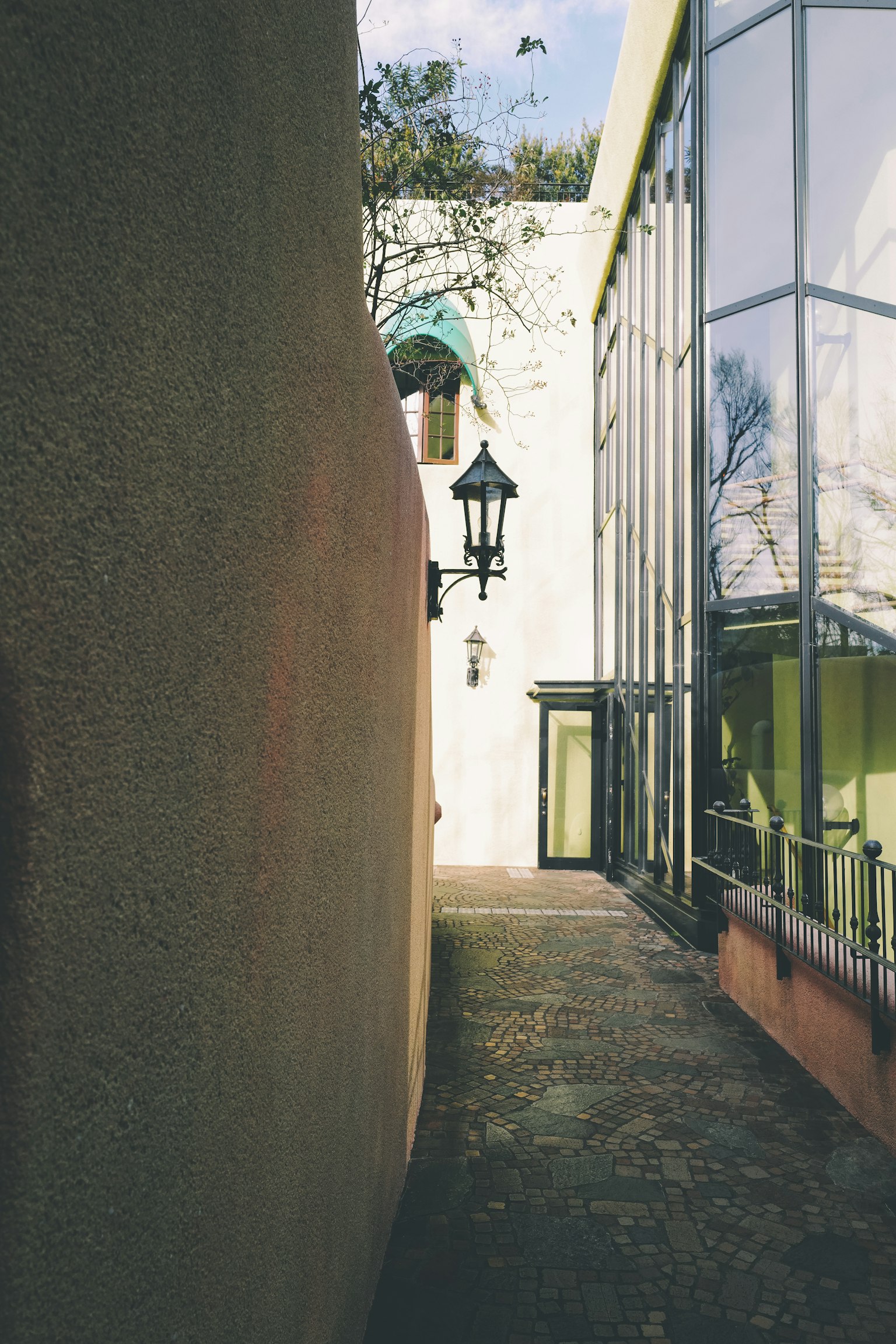 Schmaler Durchgang, flankiert von einem Glasgebäude und einer Wand