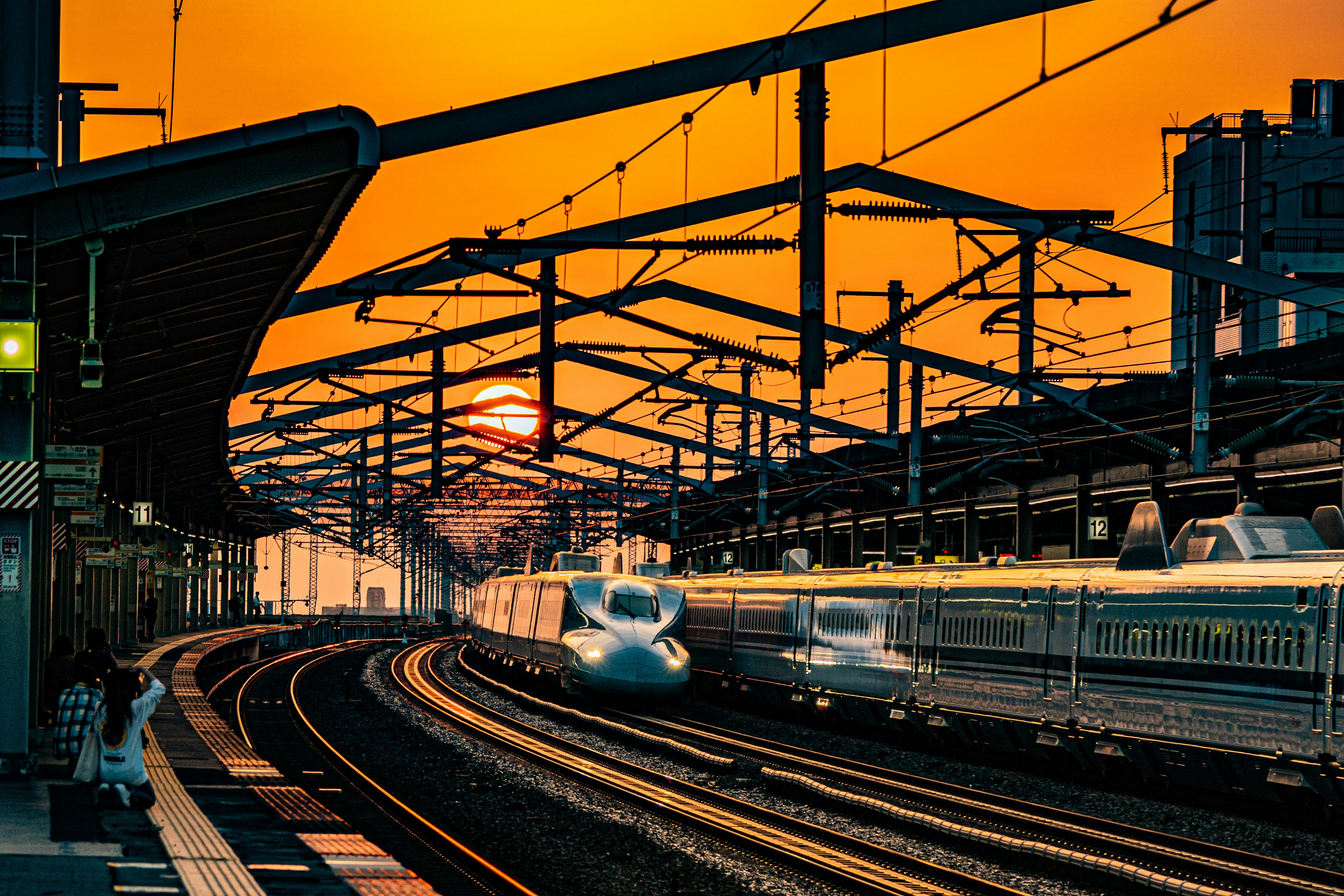 夕焼けの新幹線が高架の線路を走る反射のある駅風景