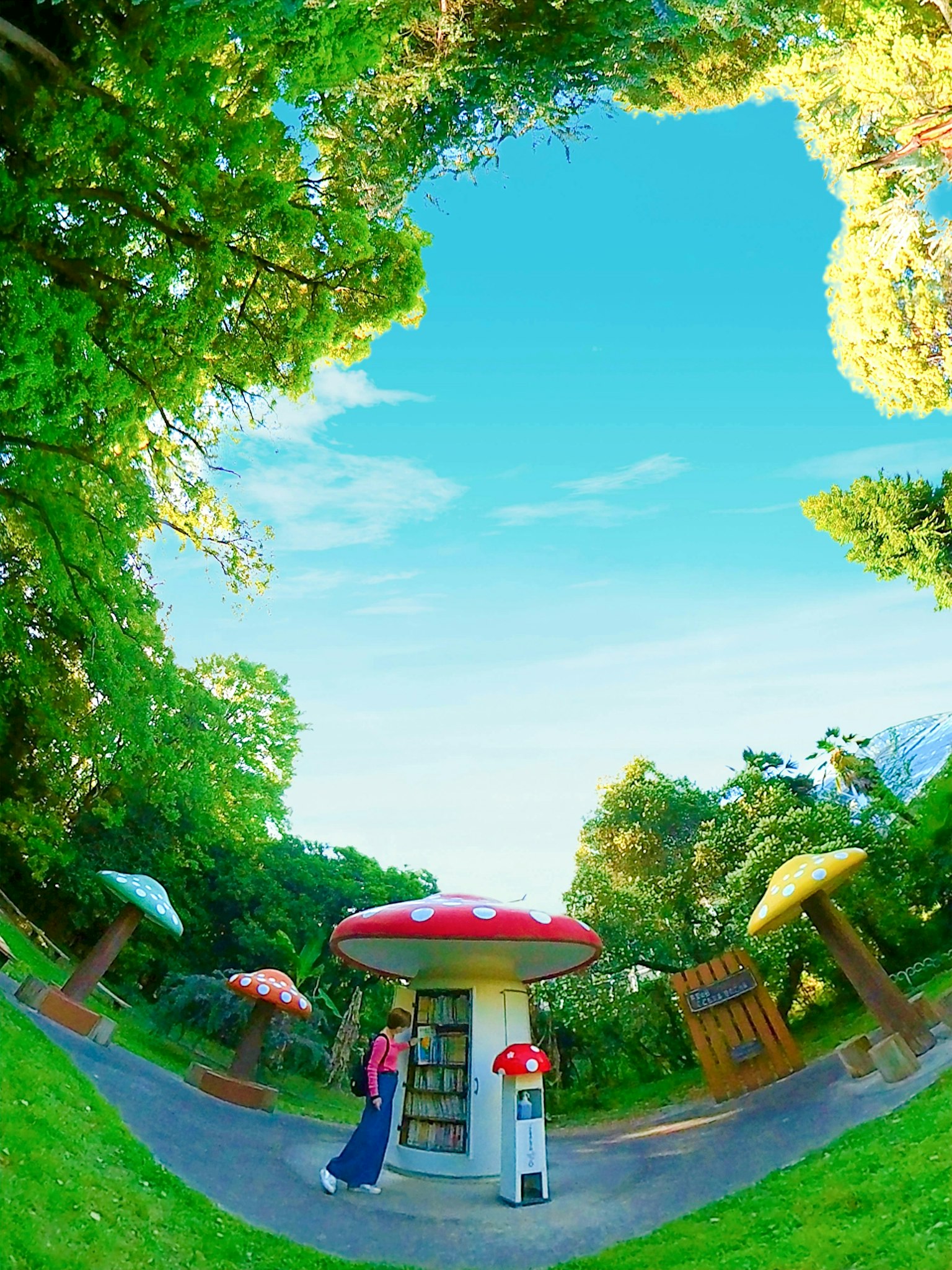 Femme se tenant sous des structures en forme de champignon colorées dans un parc verdoyant sous un ciel bleu