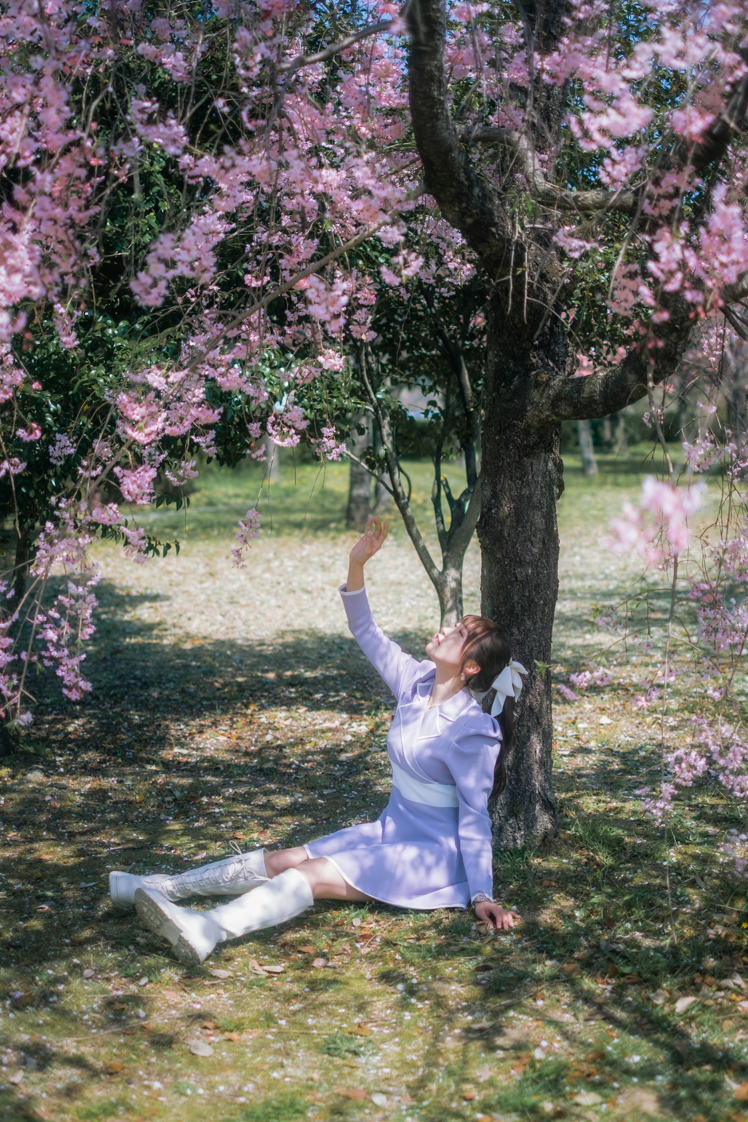 Una mujer posando bajo un árbol de cerezo en flor con un vestido púrpura claro