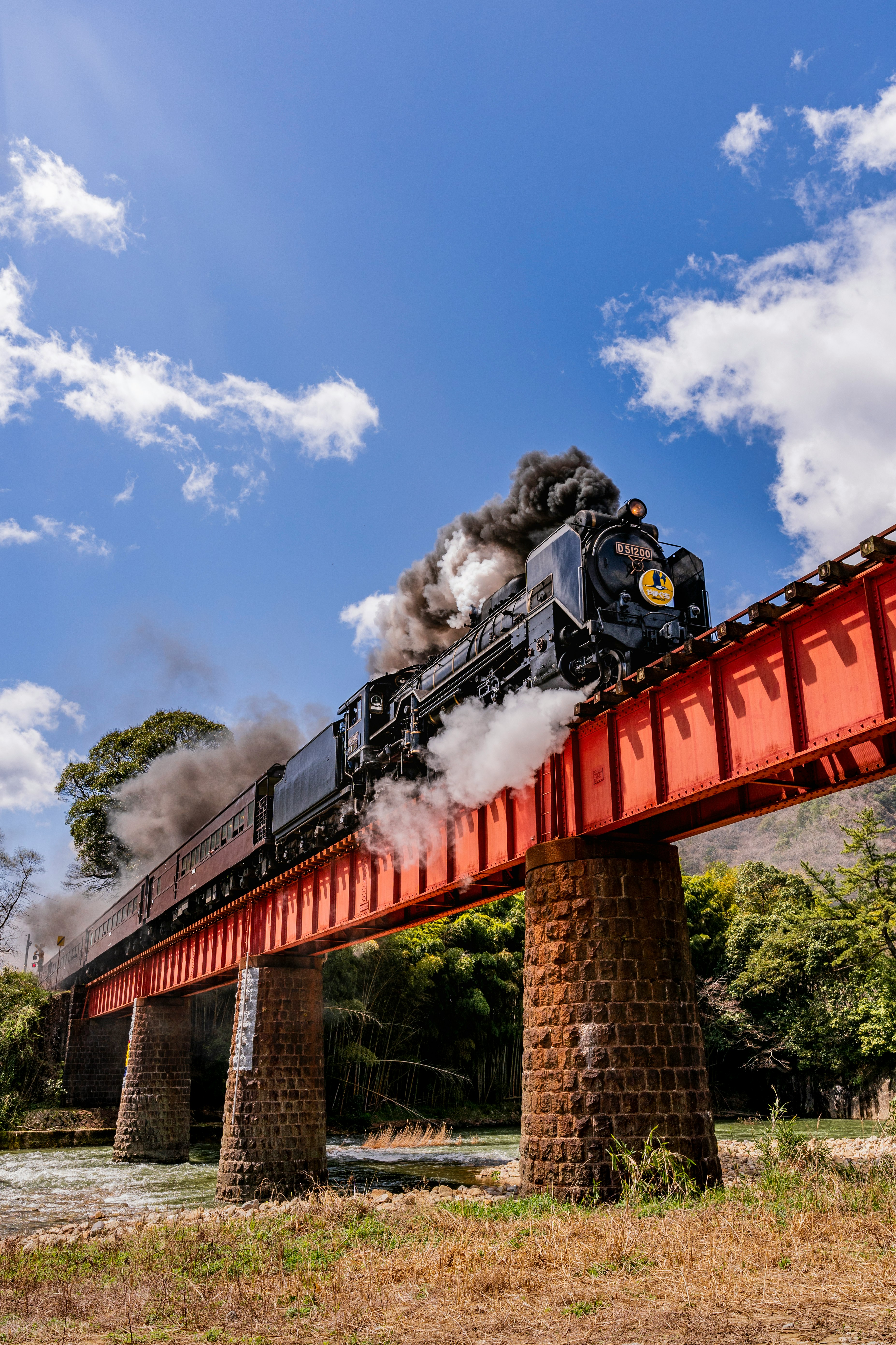 steam locomotive crossing a bridge with billowing smoke under a blue sky