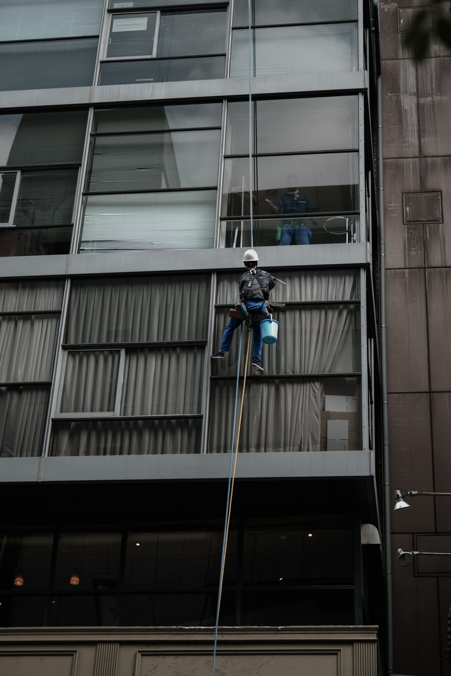 Ouvrier nettoyant les fenêtres en descendant sur une corde d'un bâtiment moderne
