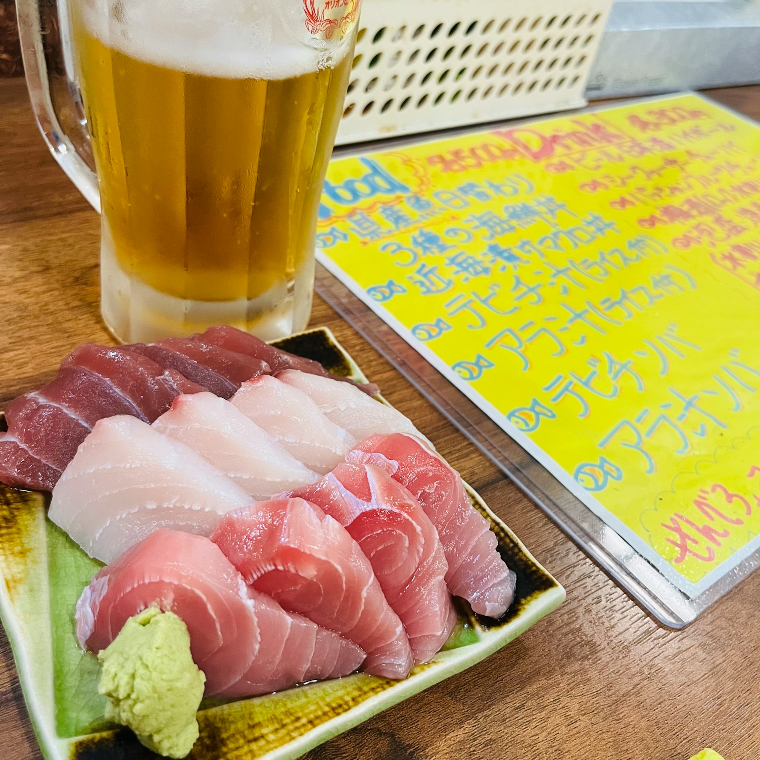 A plate of assorted sashimi with a beer on the table bright menu in the background
