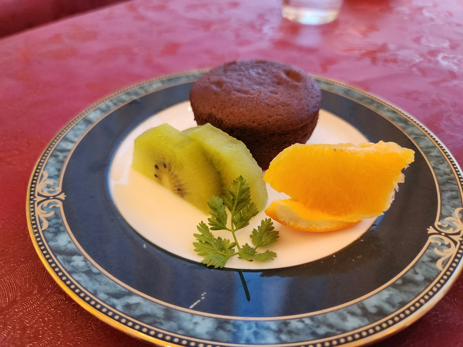 Piring dengan muffin coklat disertai irisan kiwi dan potongan jeruk dihias dengan daun ketumbar segar