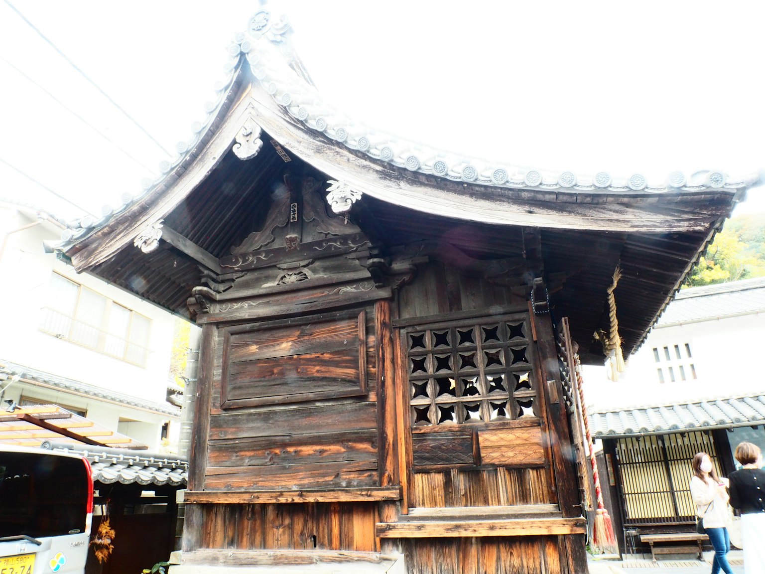 An old wooden shrine structure visible in a town small roof and decorative elements are notable