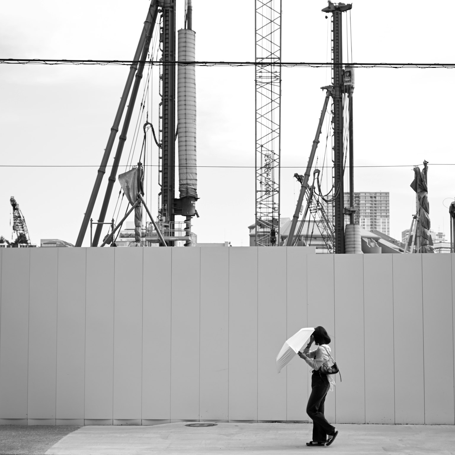 Una mujer caminando con un paraguas frente a un sitio de construcción en blanco y negro