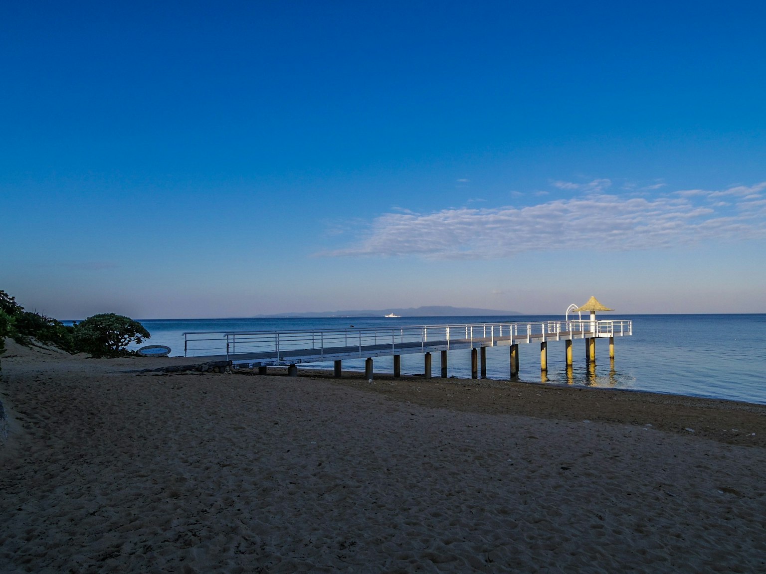 Beach scene featuring a pier extending into calm blue waters under a clear sky