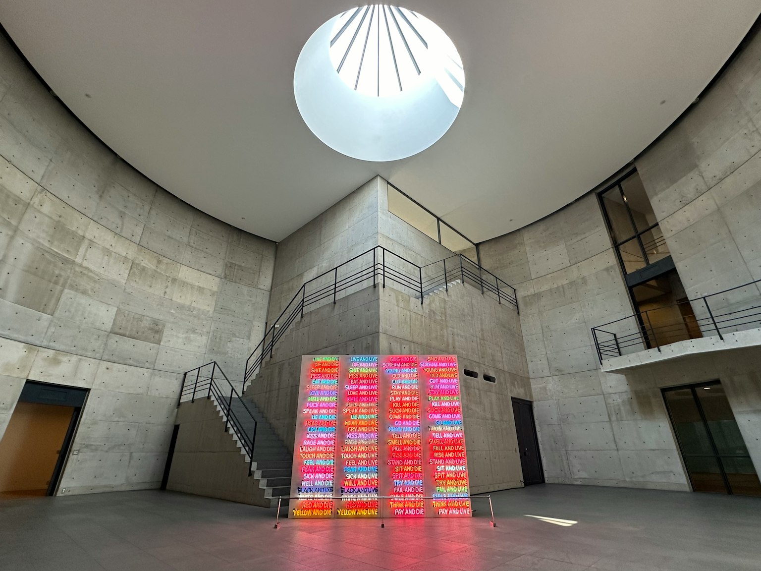 Spacious interior featuring a circular skylight and concrete walls with a colorful art installation