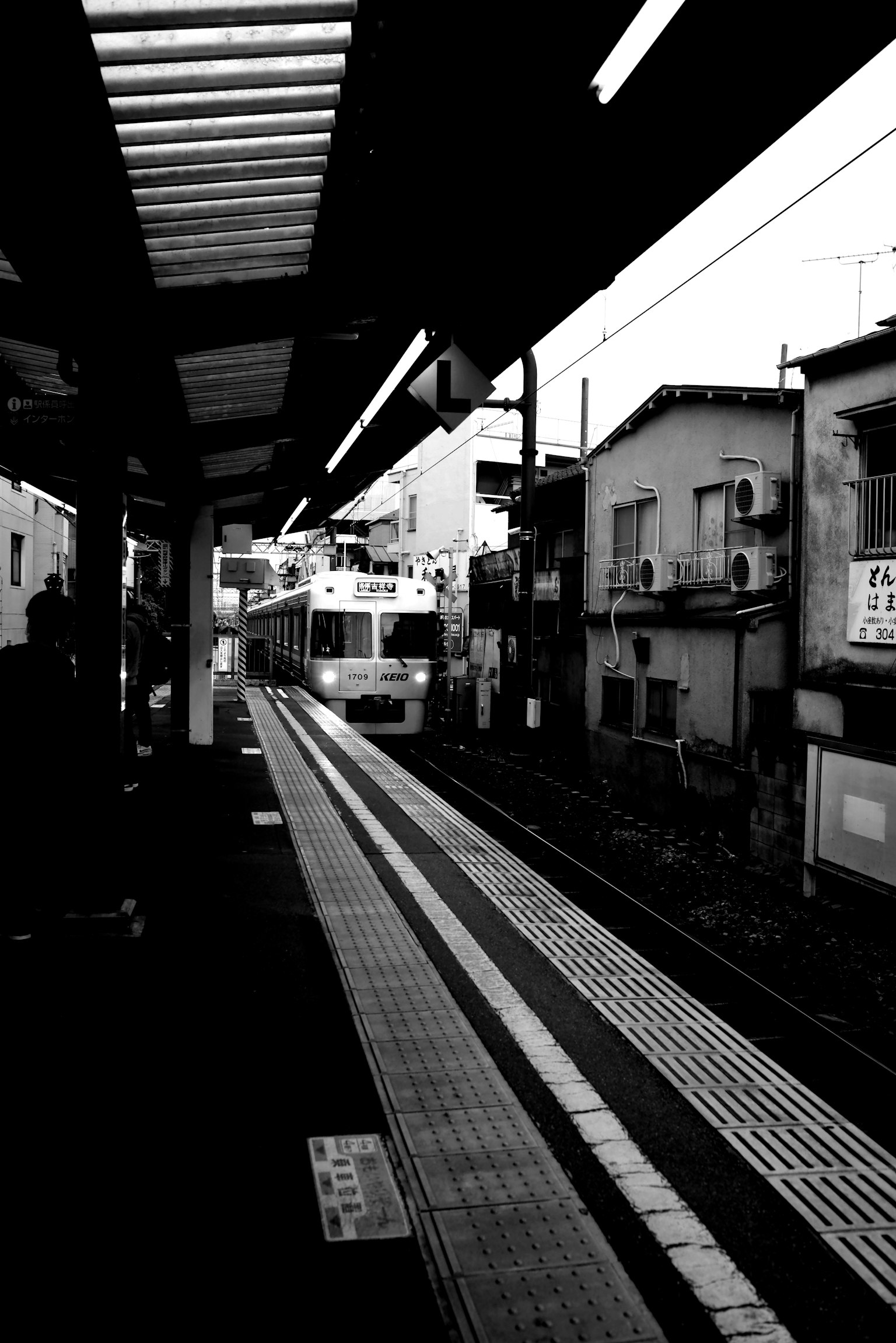 Escena en blanco y negro de un tren llegando a una estación con edificios antiguos cercanos