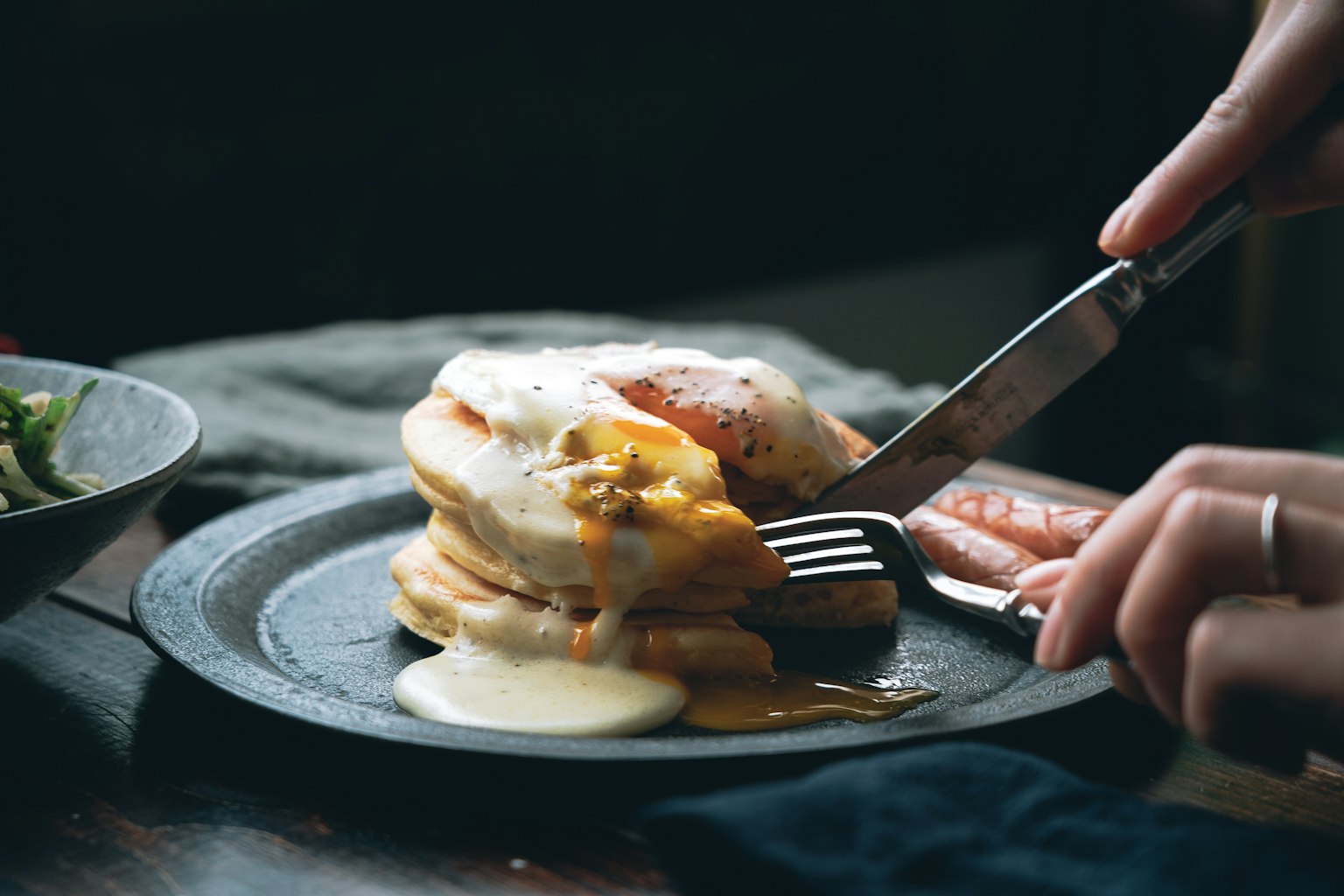 Una mano che usa una forchetta su un piatto di colazione con uova e salsiccia